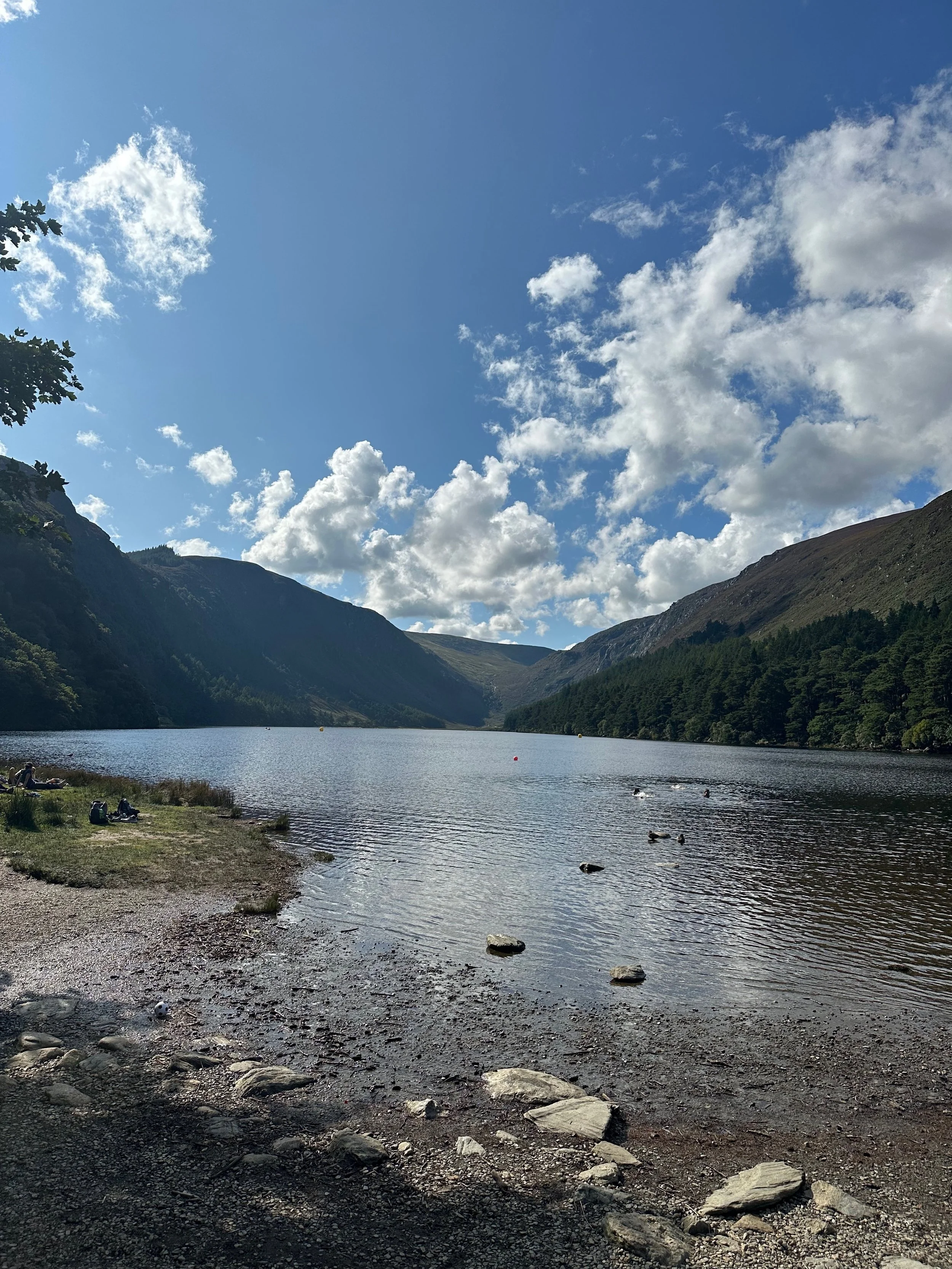 A lake surrounded by mountains with partly cloudy sky and some trees on the hillside.