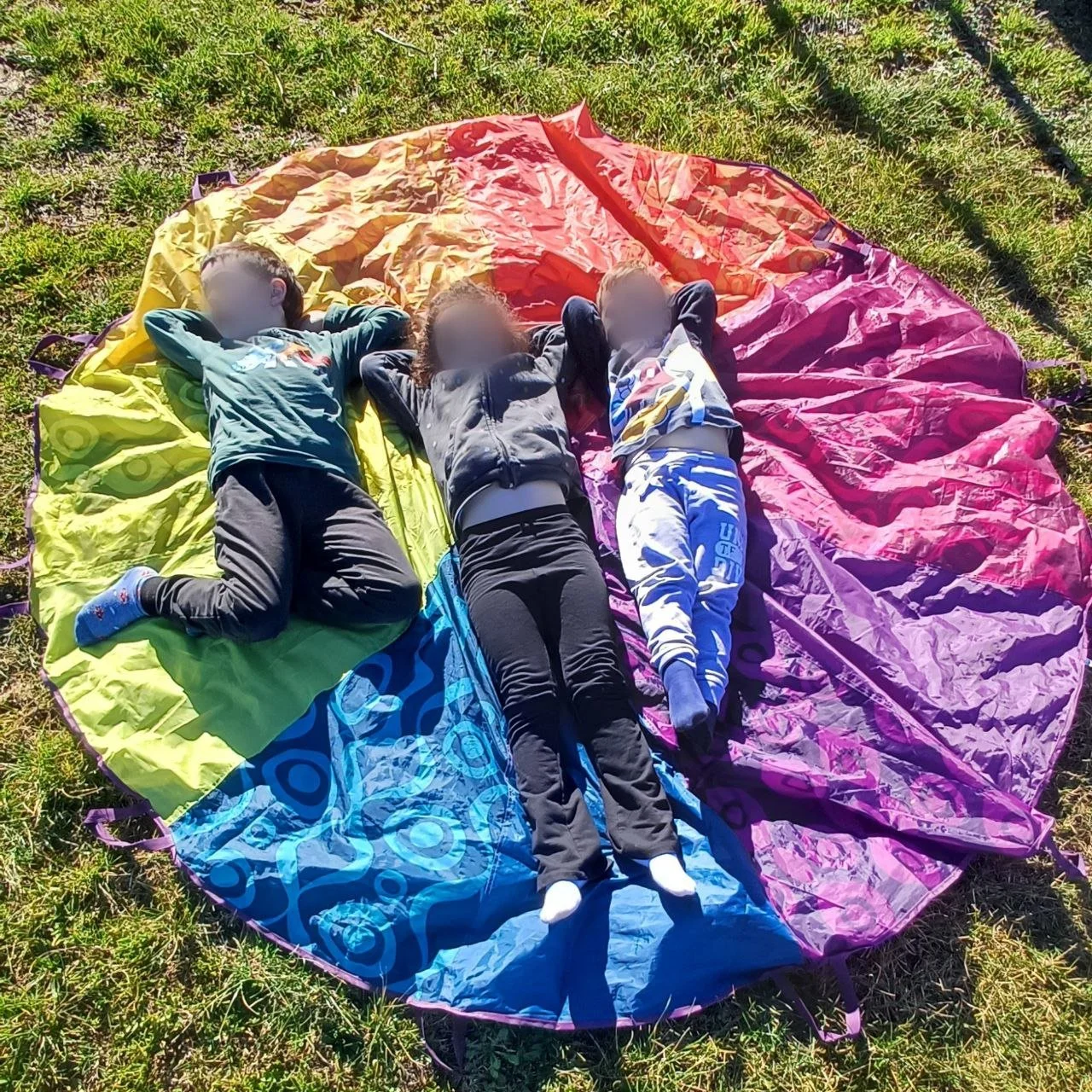 Tre bambini sdraiati su un telo colorato sulla grassa verde.