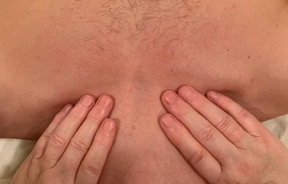 Close-up of a person's chest with hands covering the nipples.