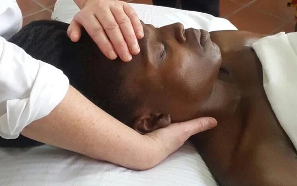 Person receiving a head massage while lying on a bed with eyes closed