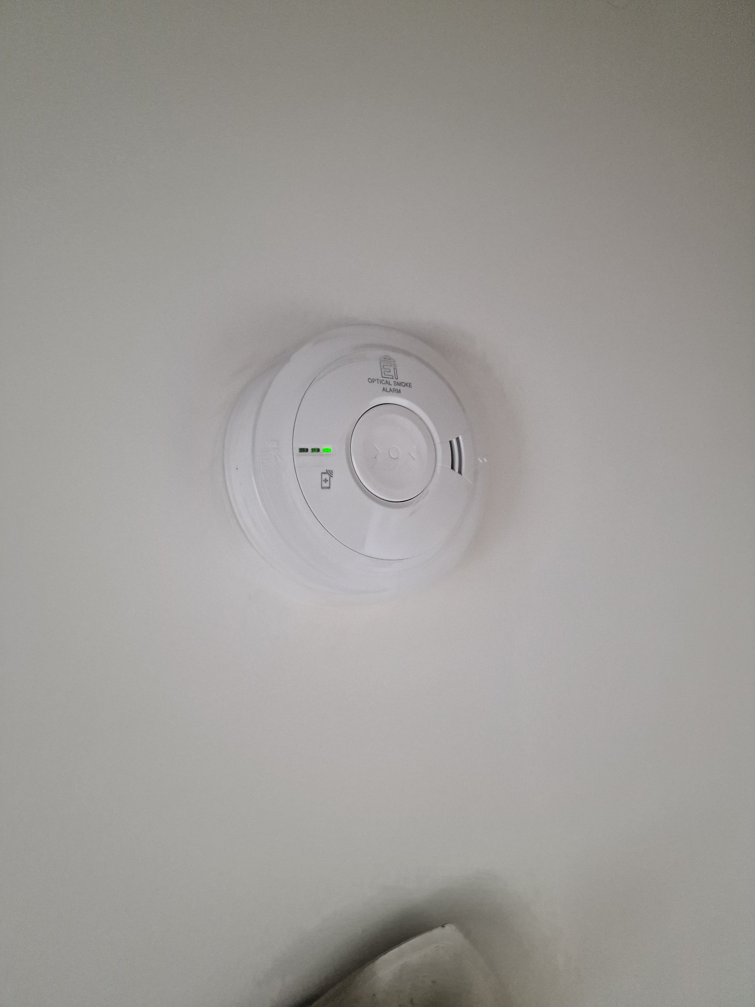 A smoke detector mounted on a ceiling with green indicator lights.