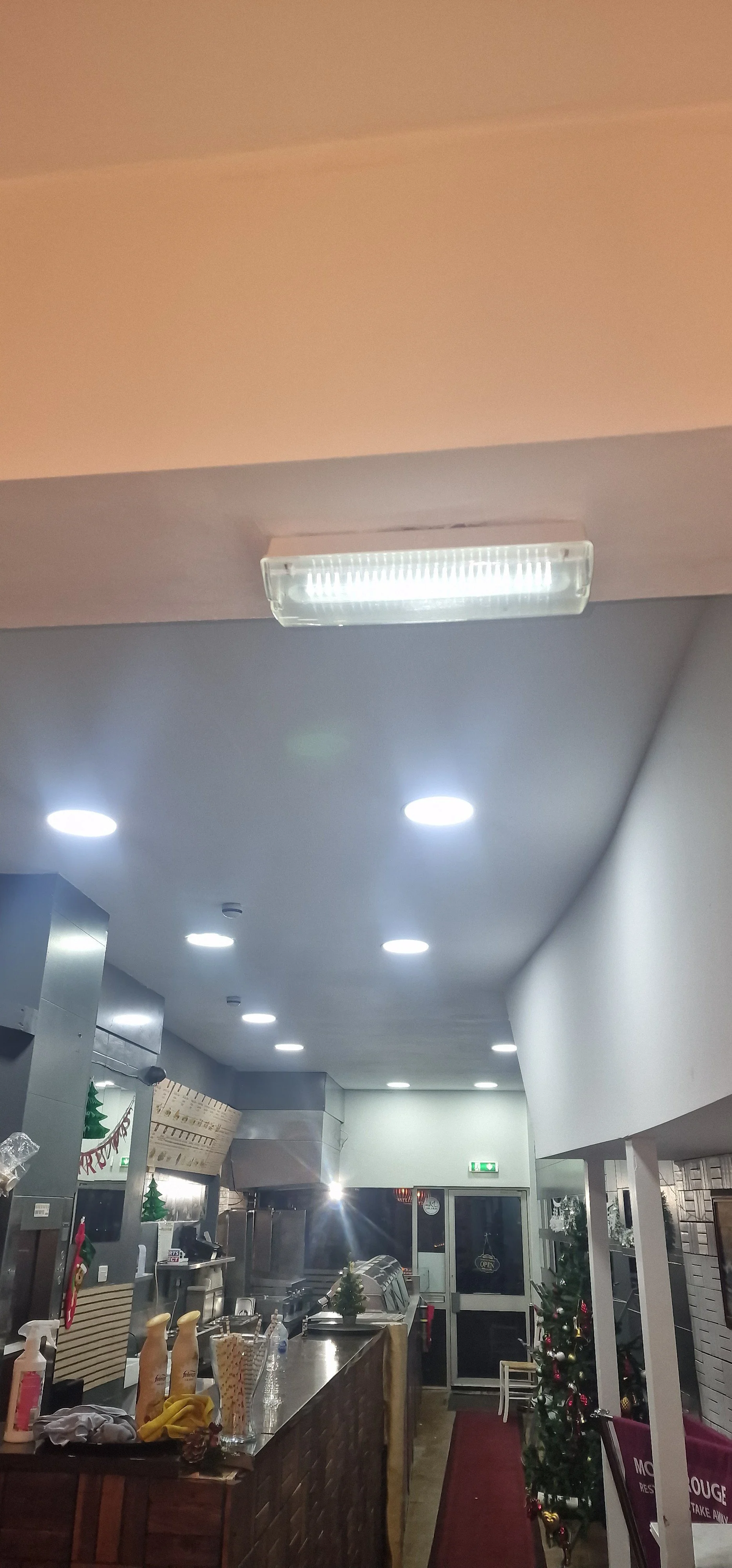 Interior of a restaurant with Christmas decorations, including a decorated Christmas tree near the entrance and small Christmas trees on the counter.