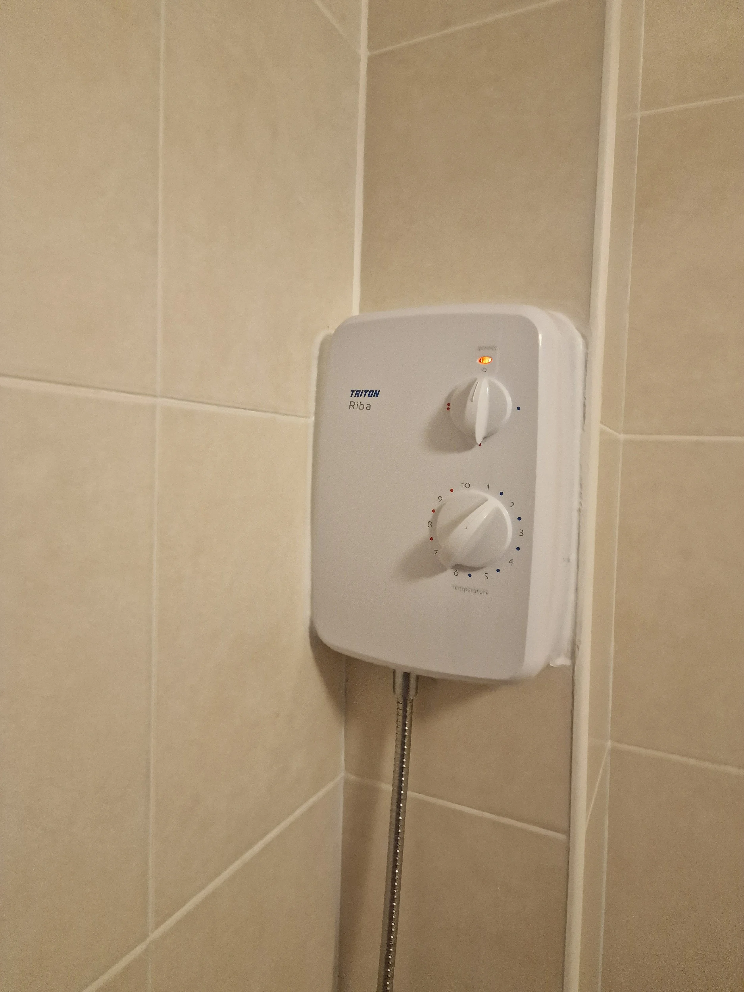 Electric shower heater mounted on bathroom wall with control knobs and orange indicator light.