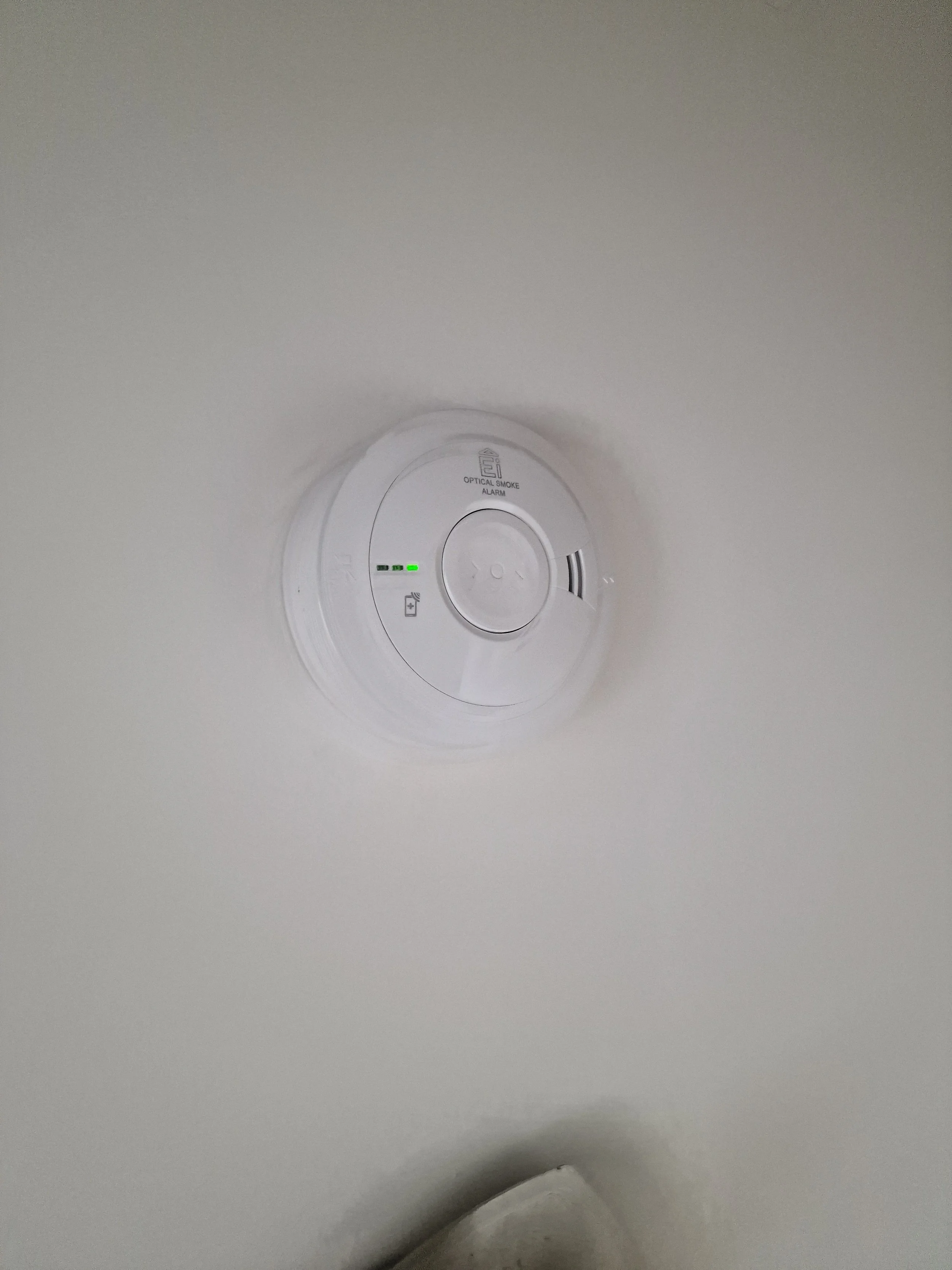 Smoke detector mounted on a white ceiling with indicator lights and test button.
