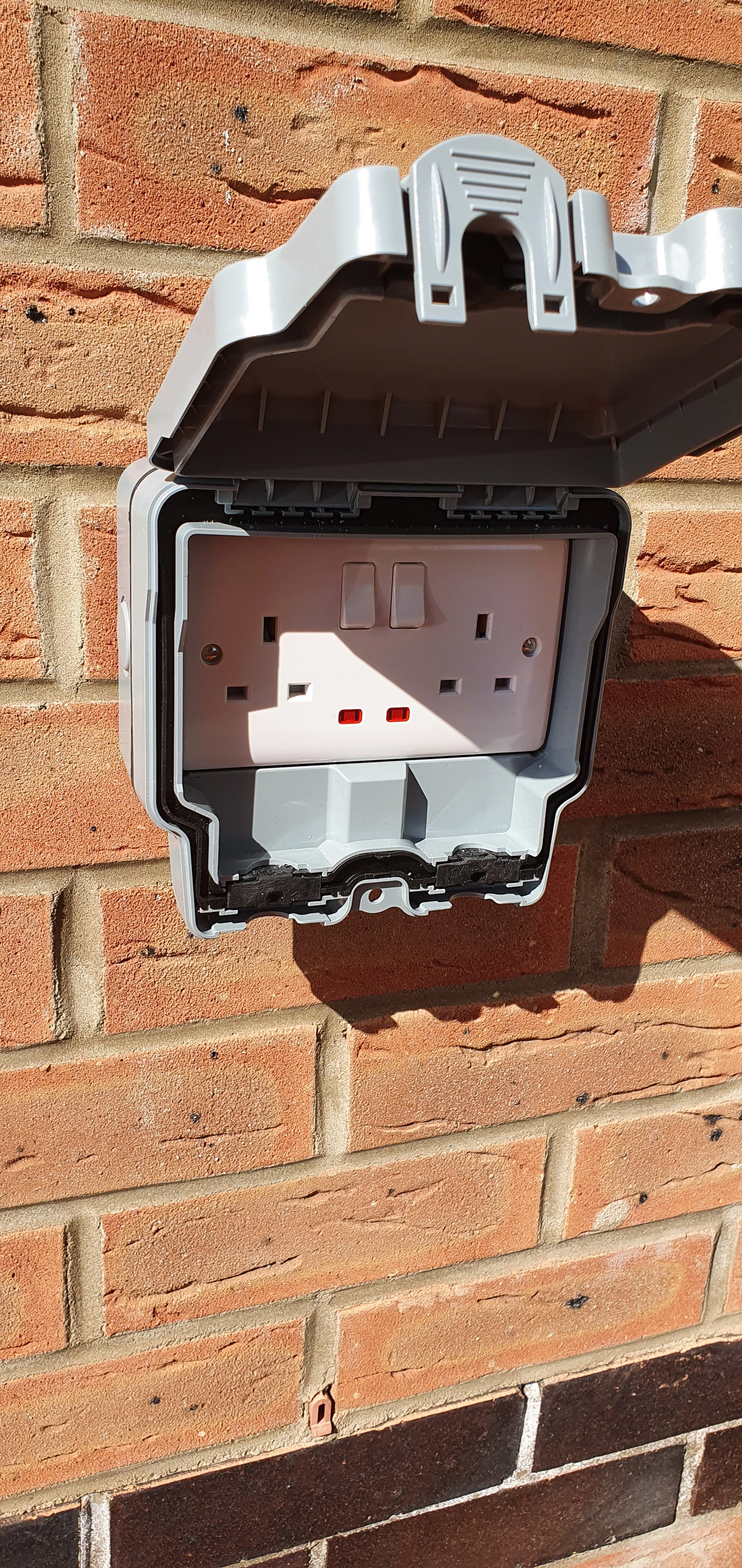Empty outdoor electrical outlet mounted on a brick wall with the cover open.