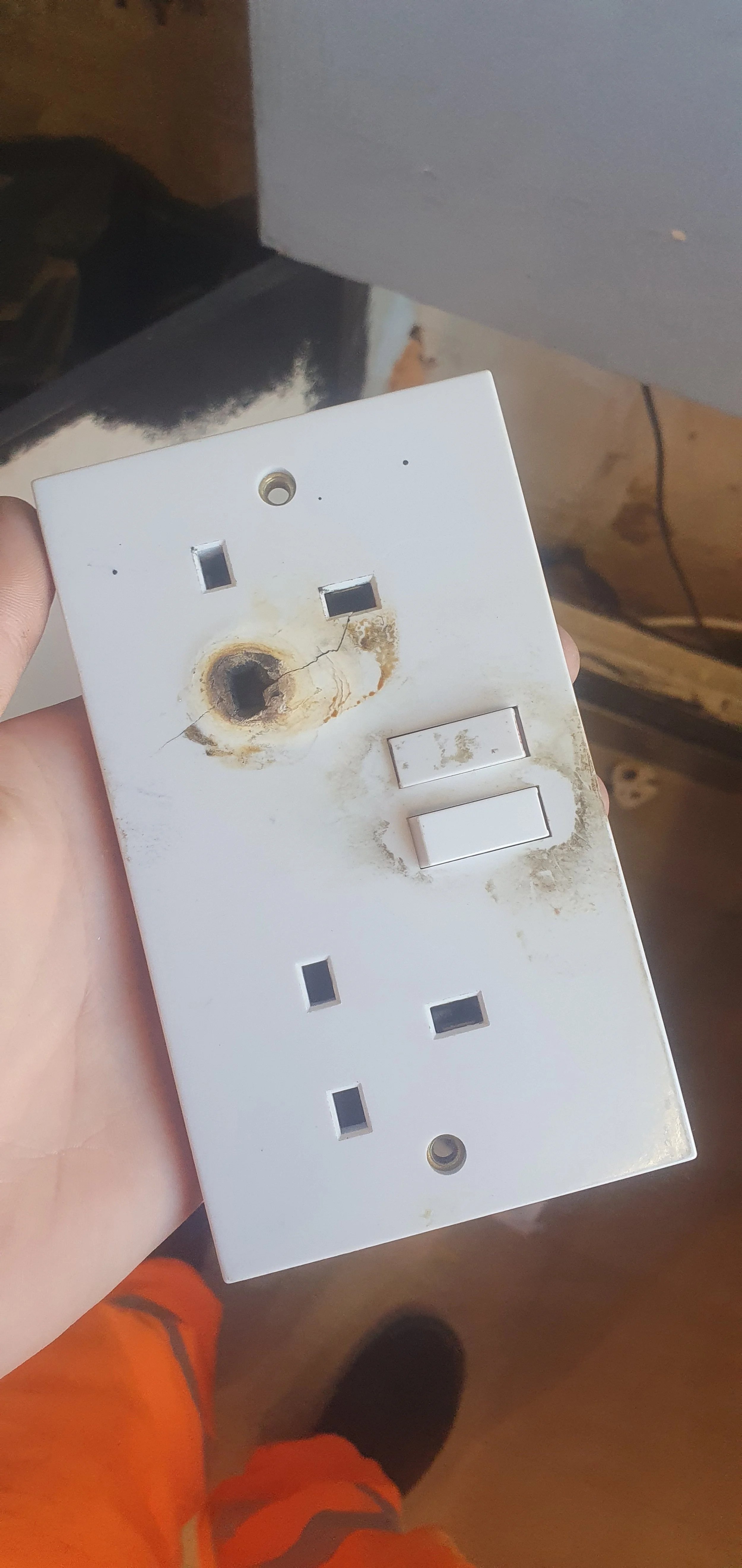 A white electrical outlet with significant burn damage and rust, missing cover plates, and scorch marks.