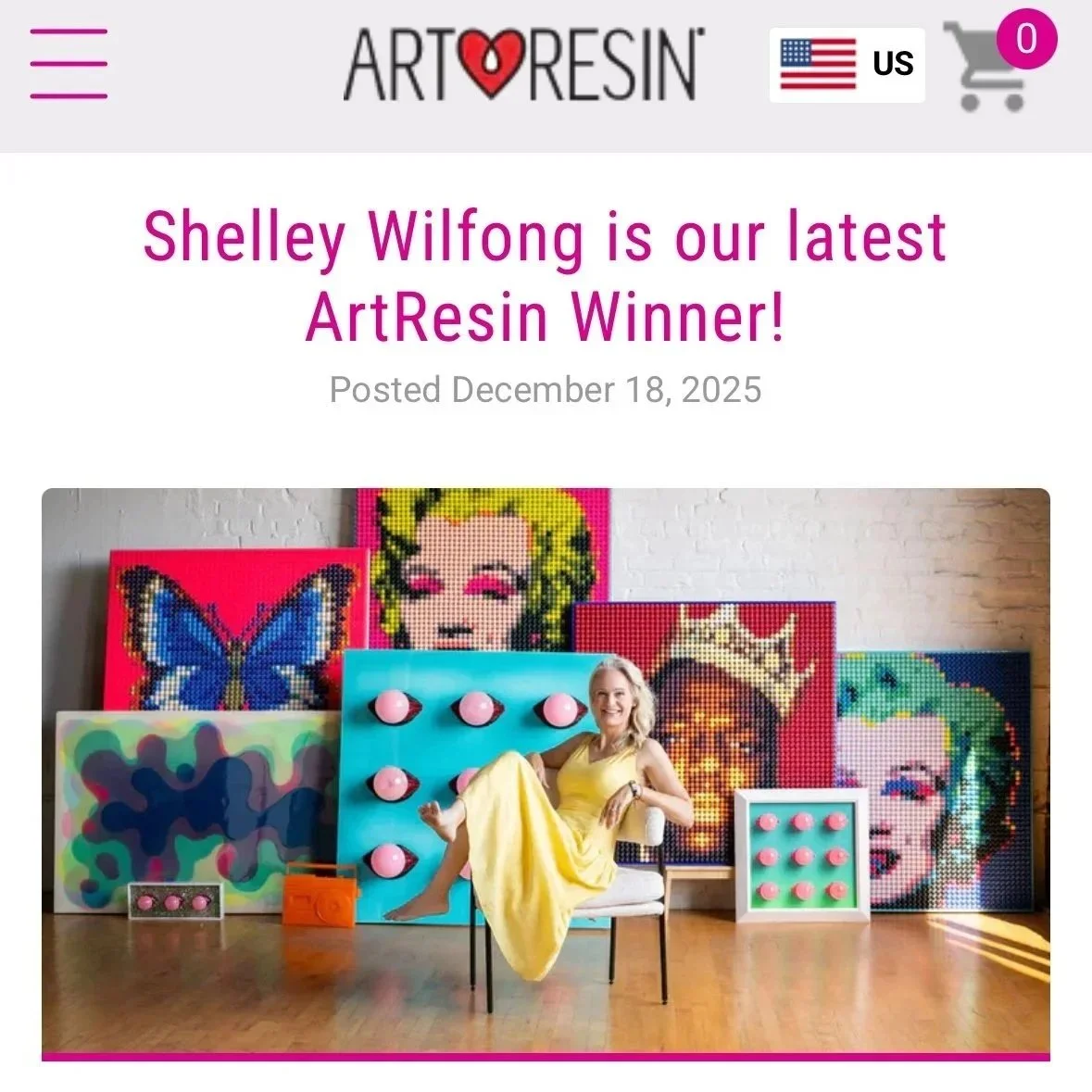 A woman in a yellow dress sitting on a chair in front of colorful artwork, including pixelated portraits, butterfly, pop art lady, and crown images, with pink buoyant balls on a blue panel and a small framed art piece with pink balls on the floor.