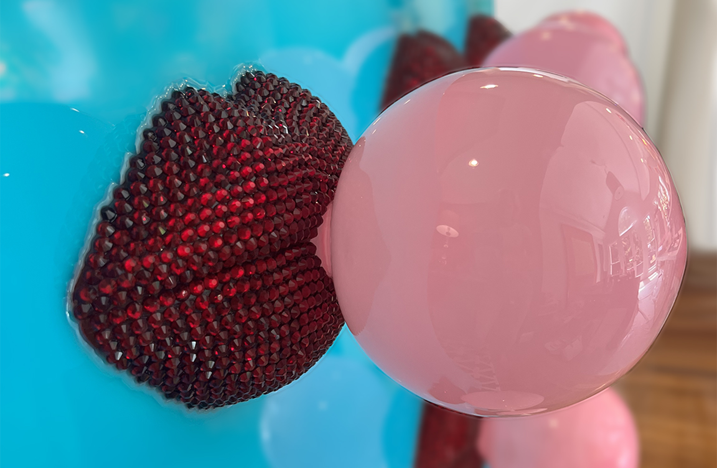 Close-up of colorful decorative objects, featuring a shiny pink spherical object and a multicolored, textured round object next to a light blue background with hints of other pink spheres.
