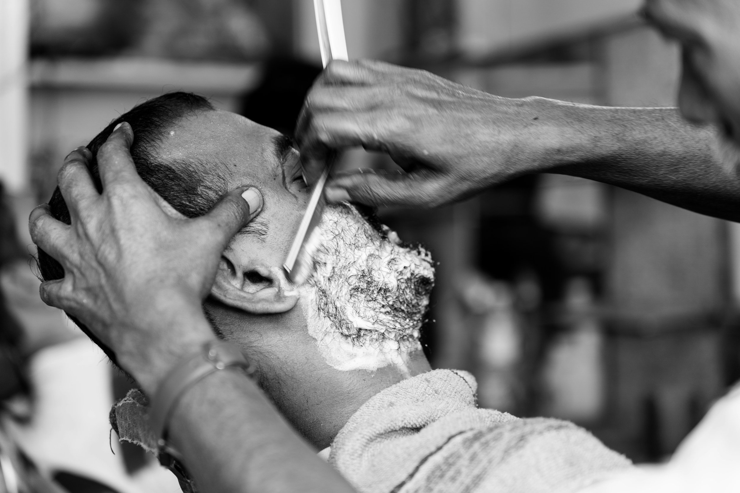 A man receiving a traditional shave, with someone applying aftershave or lotion on his face, in a barbershop setting.