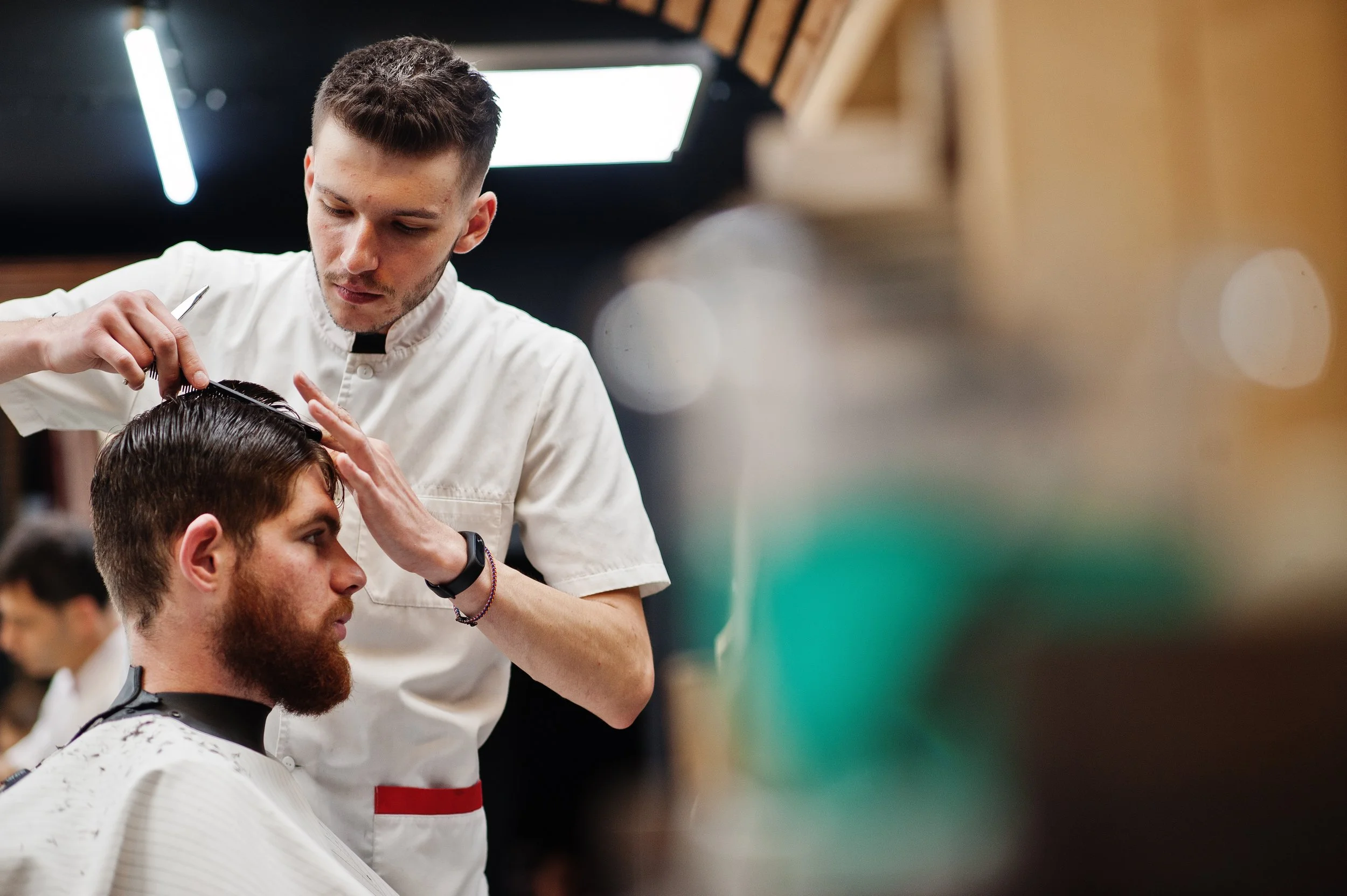 Barber giving a haircut in a barbershop with a male customer sitting in the chair.
