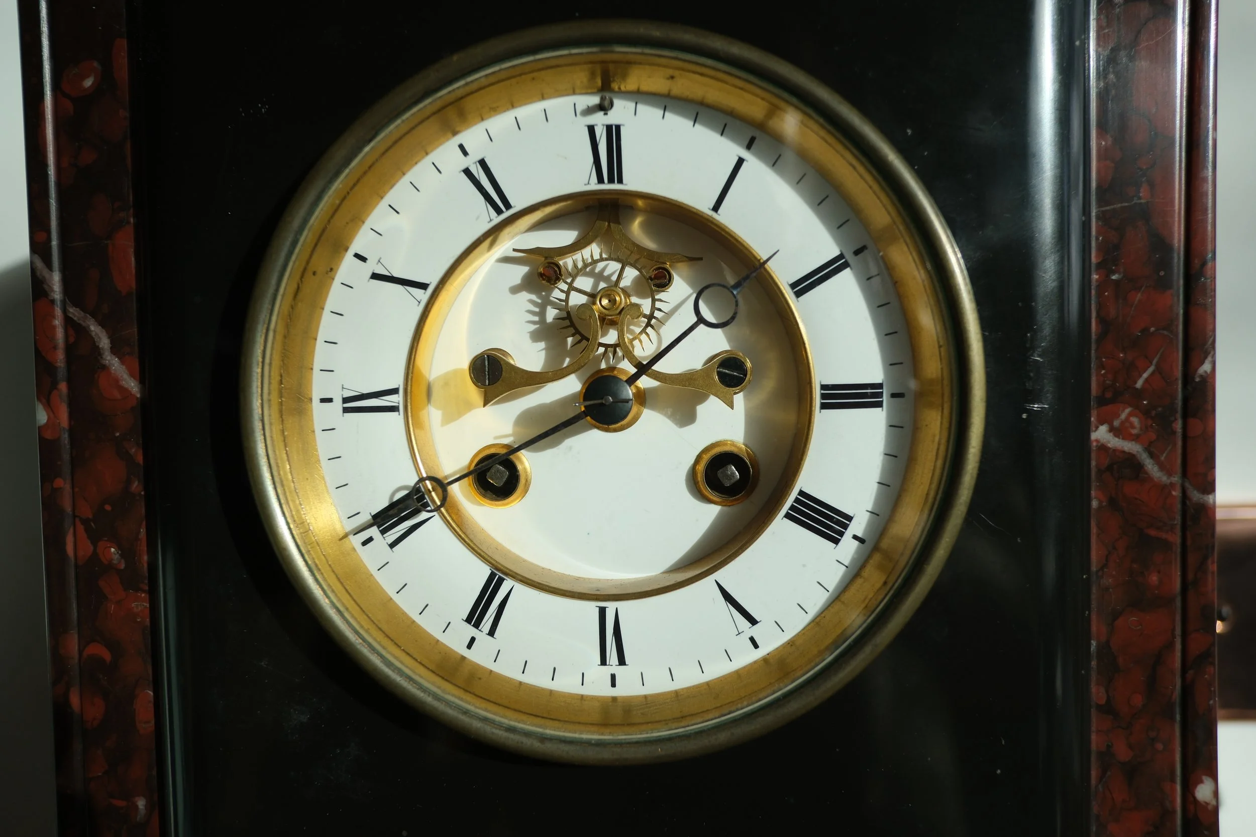 An antique clock with a white face, Roman numerals, and gold accents, displaying the time as approximately 10:07.