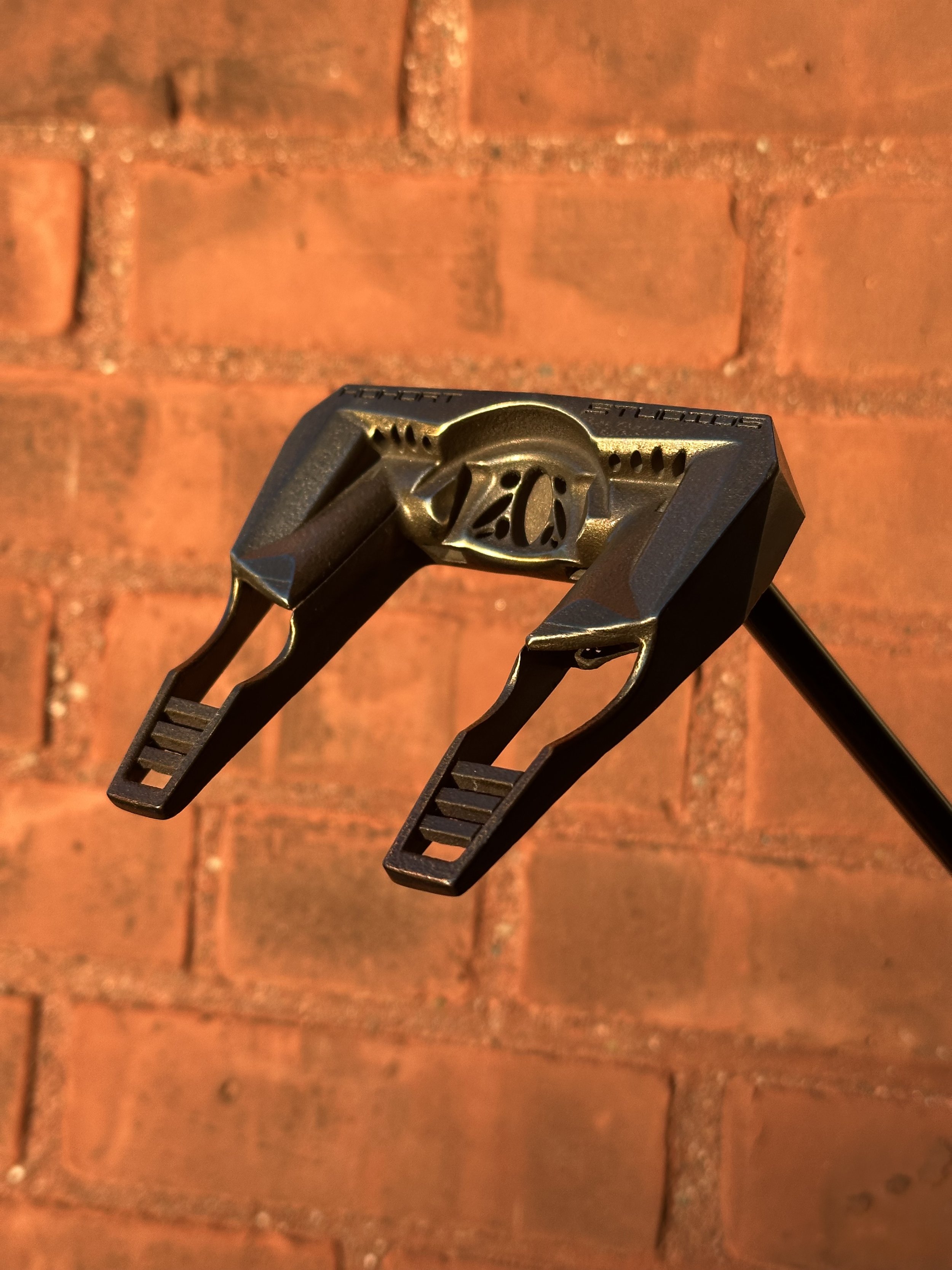 A golf ball teeing device with a 20-yard marker, set against a red brick wall.