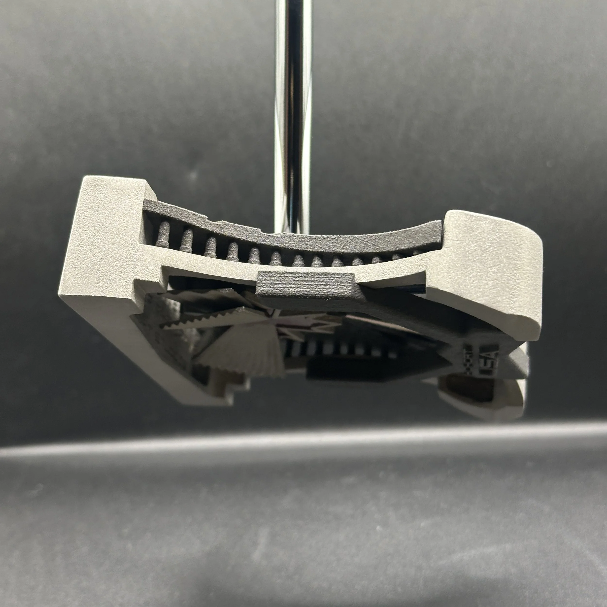 Close-up of an adjustable bicycle seat clamp attached to a bike seat post, with a textured gray and black color scheme, against a gray background.