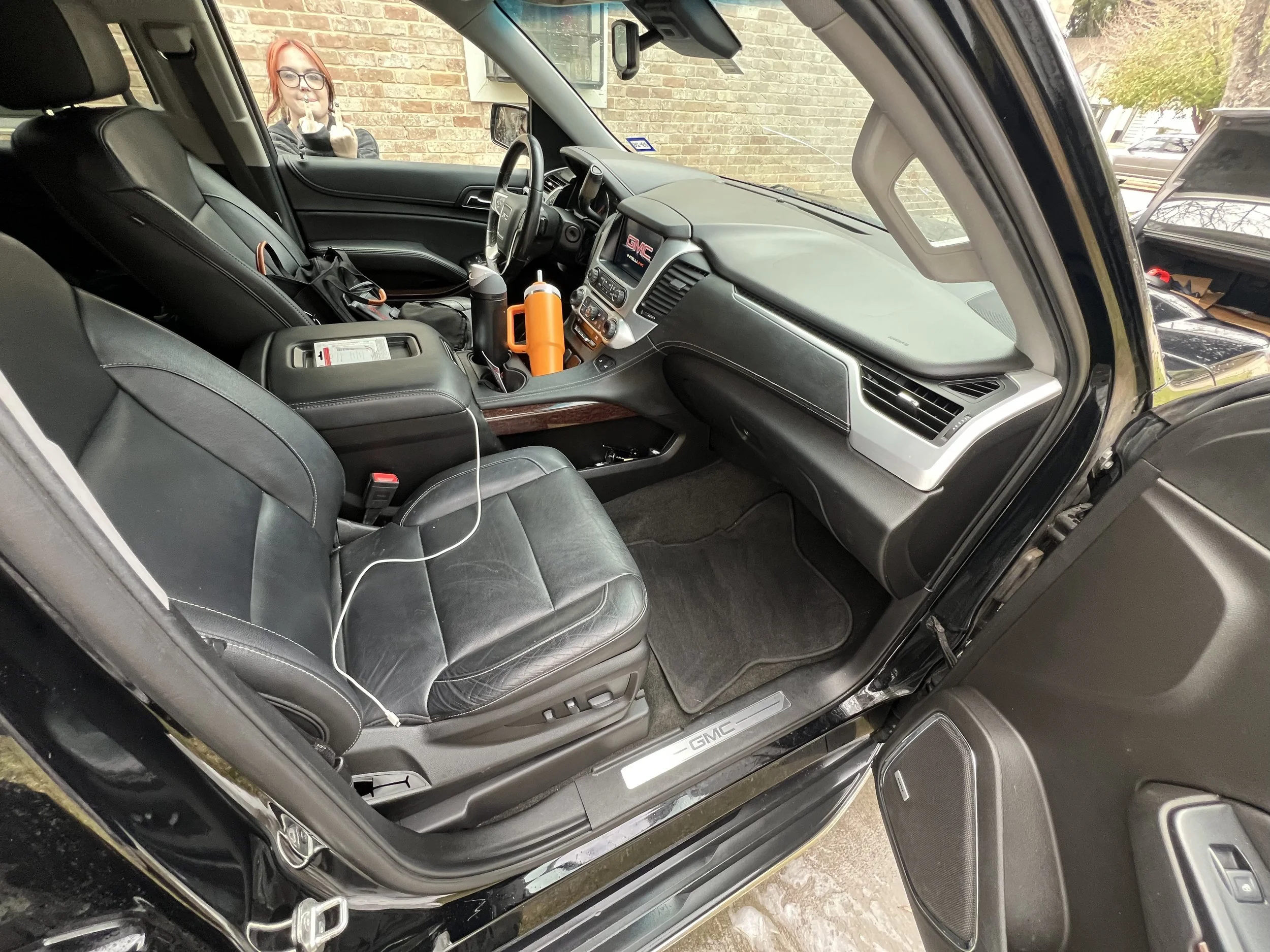 The interior of a black GMC vehicle showing front seats, dashboard with GM logo, and various items like orange bottles and a charging cable inside.