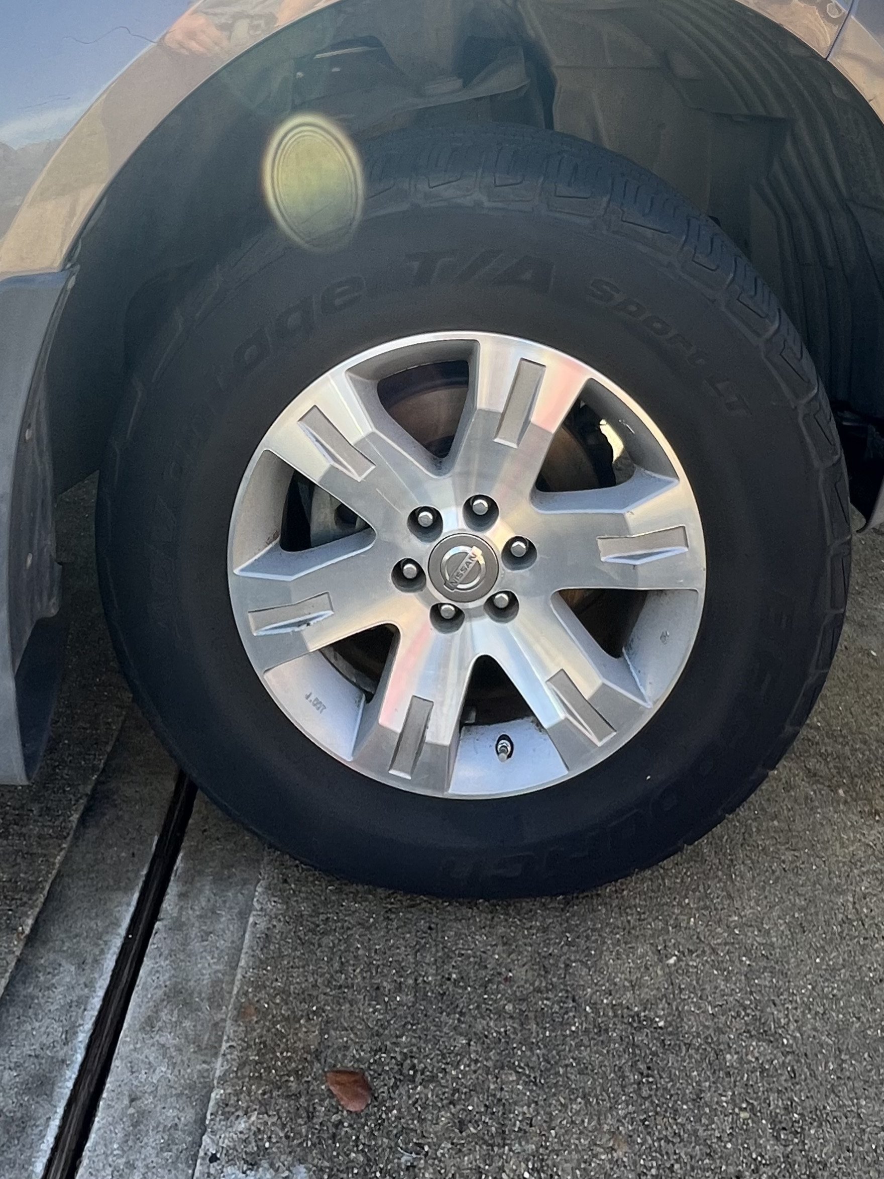 Close-up of a car tire and silver alloy wheel with Nissan emblem on the hubcap, parked on asphalt.