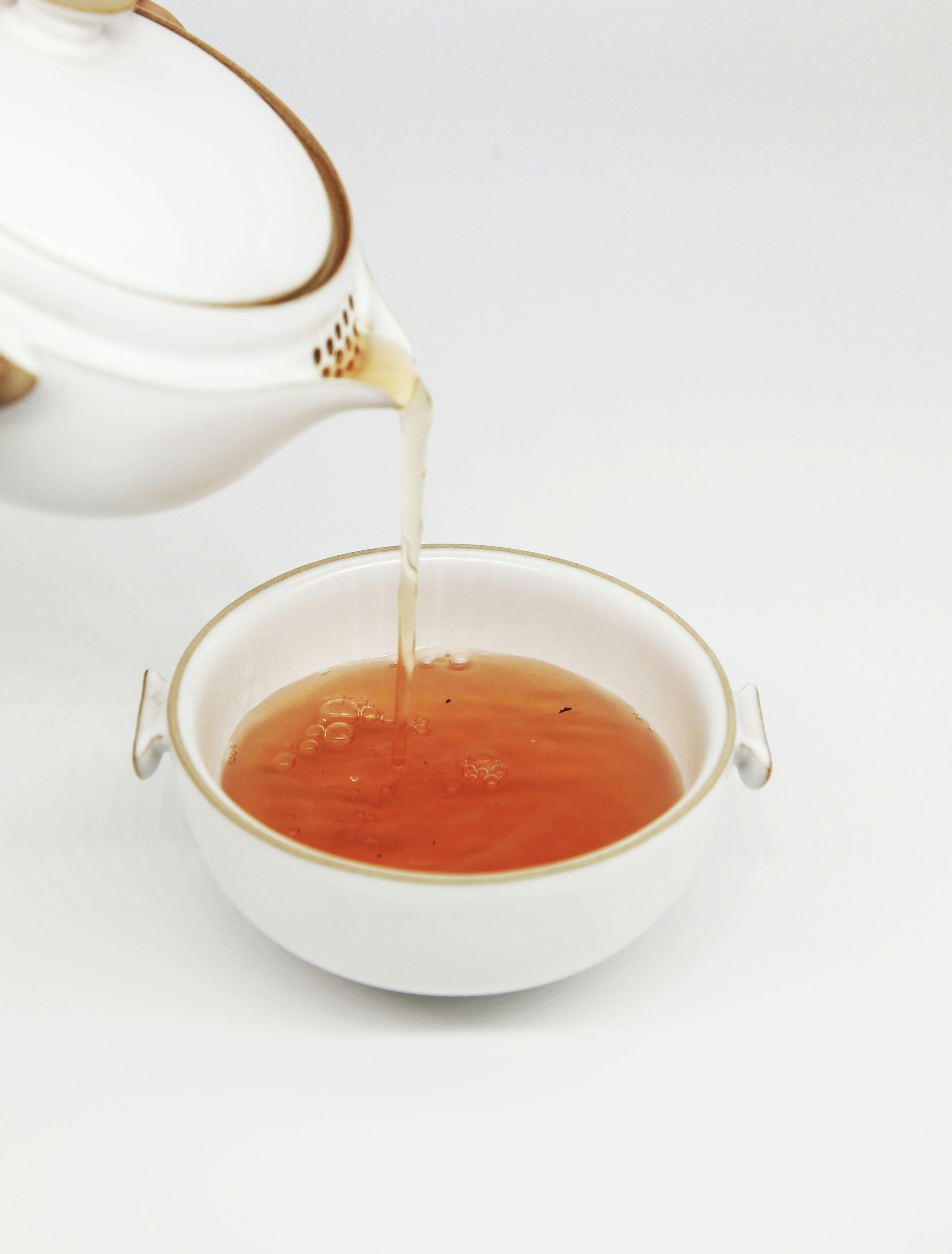 Tea being poured from a teapot into a white cup on a white background.