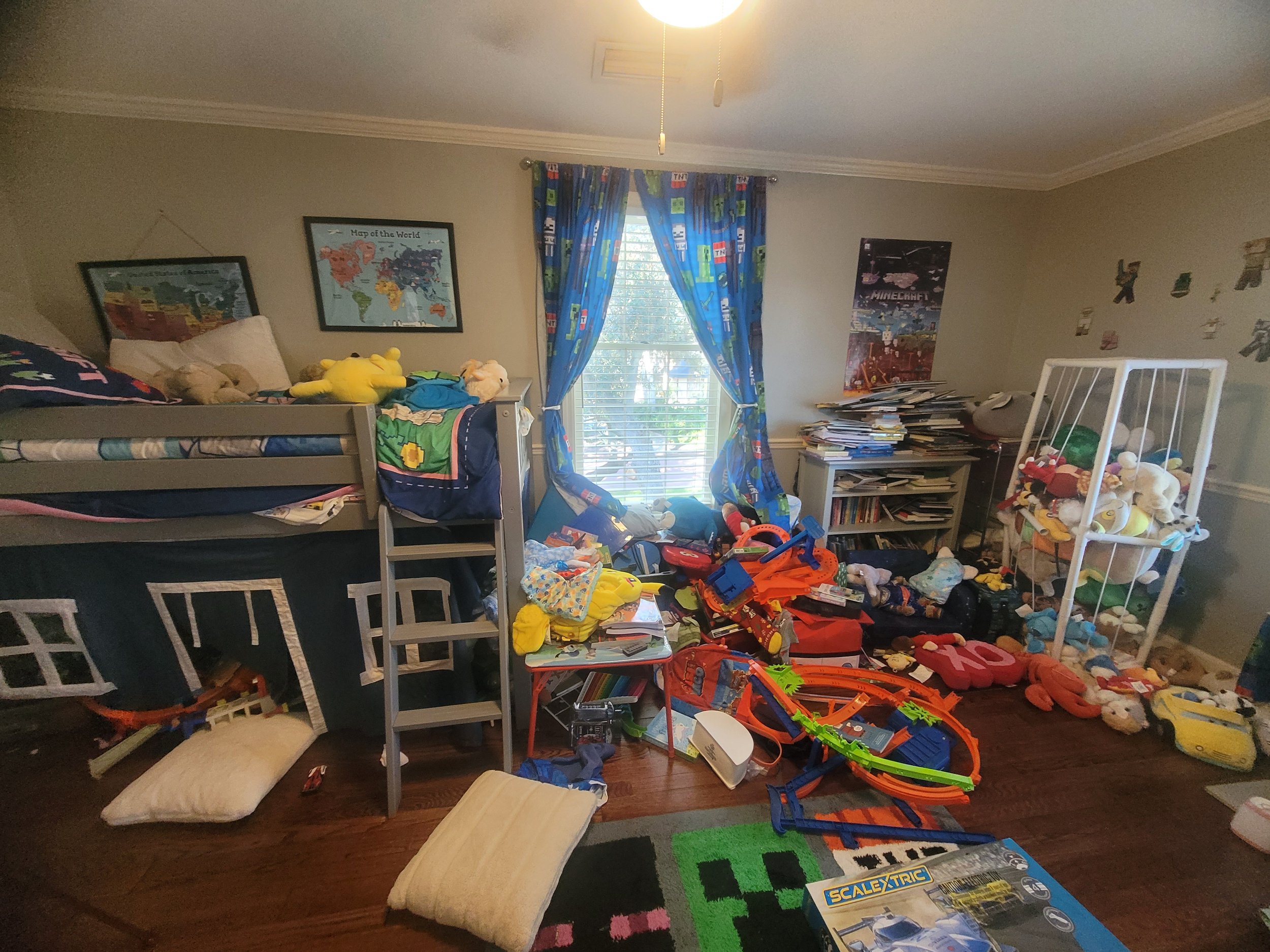 Cluttered child's bedroom with bunk bed, scattered toys, books, and posters on the walls, and window with colorful curtains.