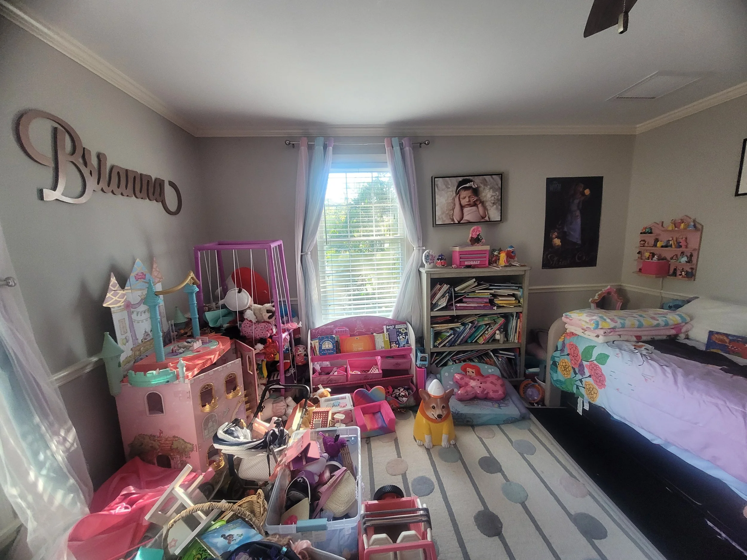 A child's bedroom with a window, bookshelf, decorated bed, and an assortment of toys and stuffed animals scattered around the room, including a toy dog figure on the floor.