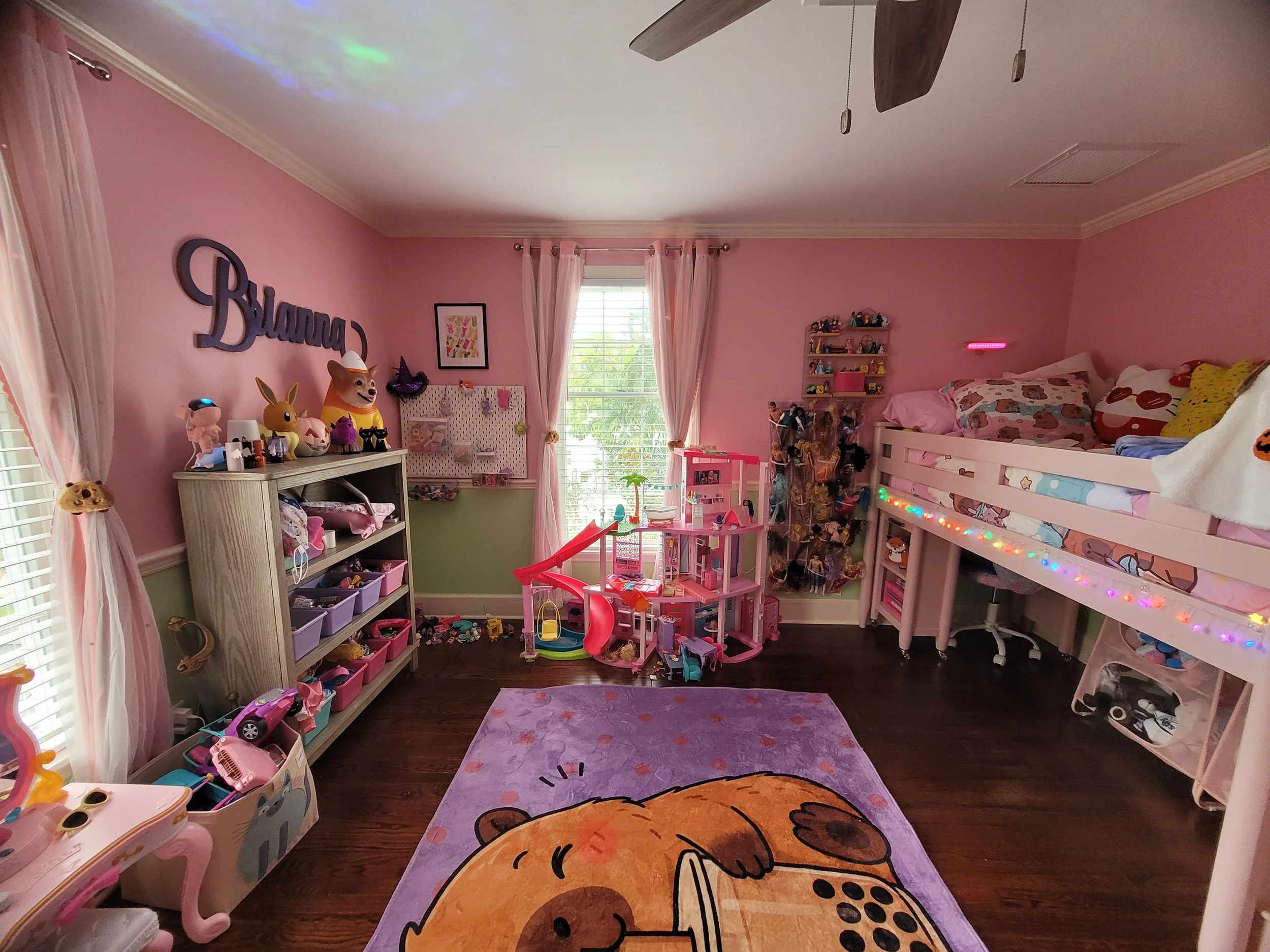 A pink-themed children's bedroom with toys, a bed, shelves, and a window with pink curtains.