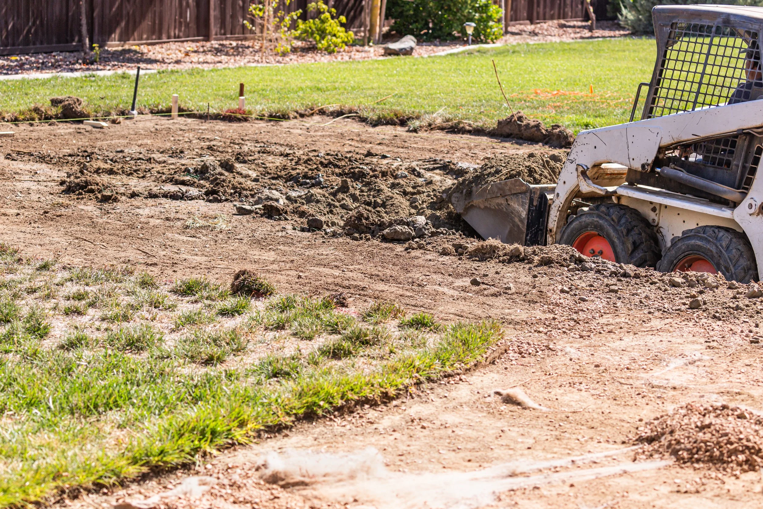 A small construction digger in a backyard, removing soil for landscaping or a foundation.