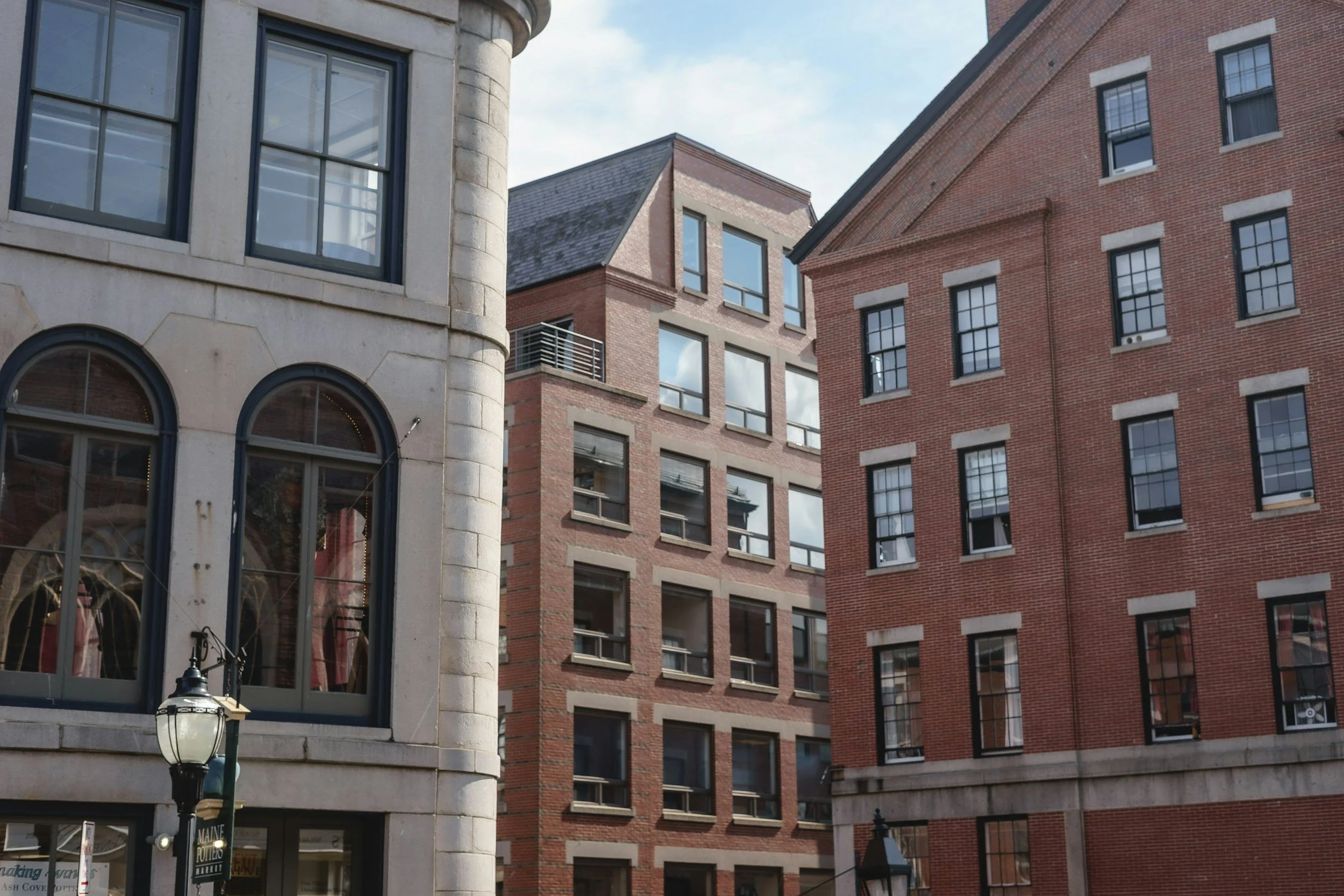 Several multi-story brick and stone buildings with large windows in a city setting under a partly cloudy sky.