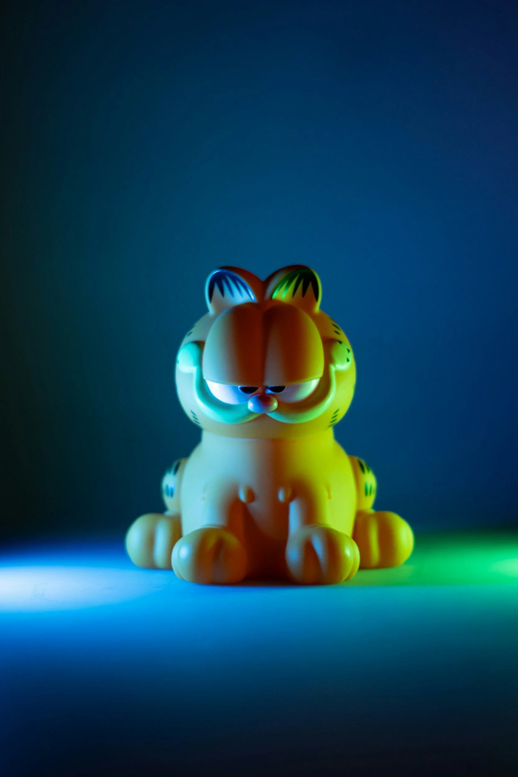 A yellow Garfield plush toy illuminated by colorful lights in a dark setting