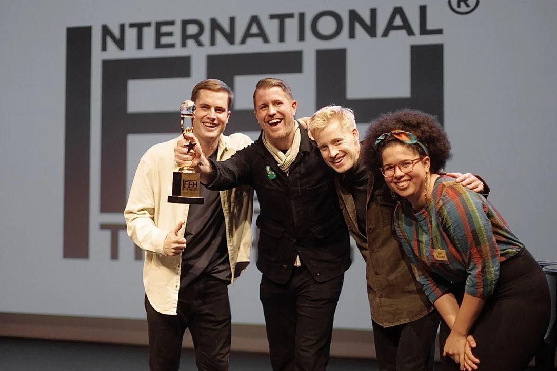 Four people on stage celebrating, with one holding a trophy, at an event titled 'International FFH'.