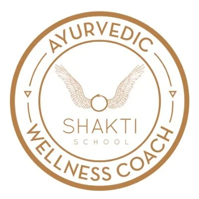 Logo for Shakti School featuring a circular design with the words 'Ayurvedic Wellness Coach' and a pair of wings connected by a ring, with 'Shakti School' in the center.