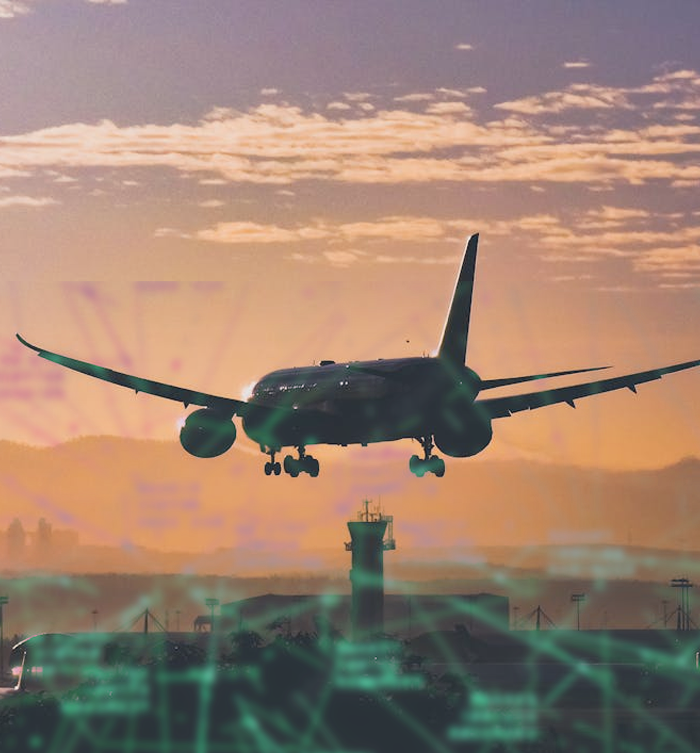 An airplane descending toward an airport runway at sunset with a control tower in the background.