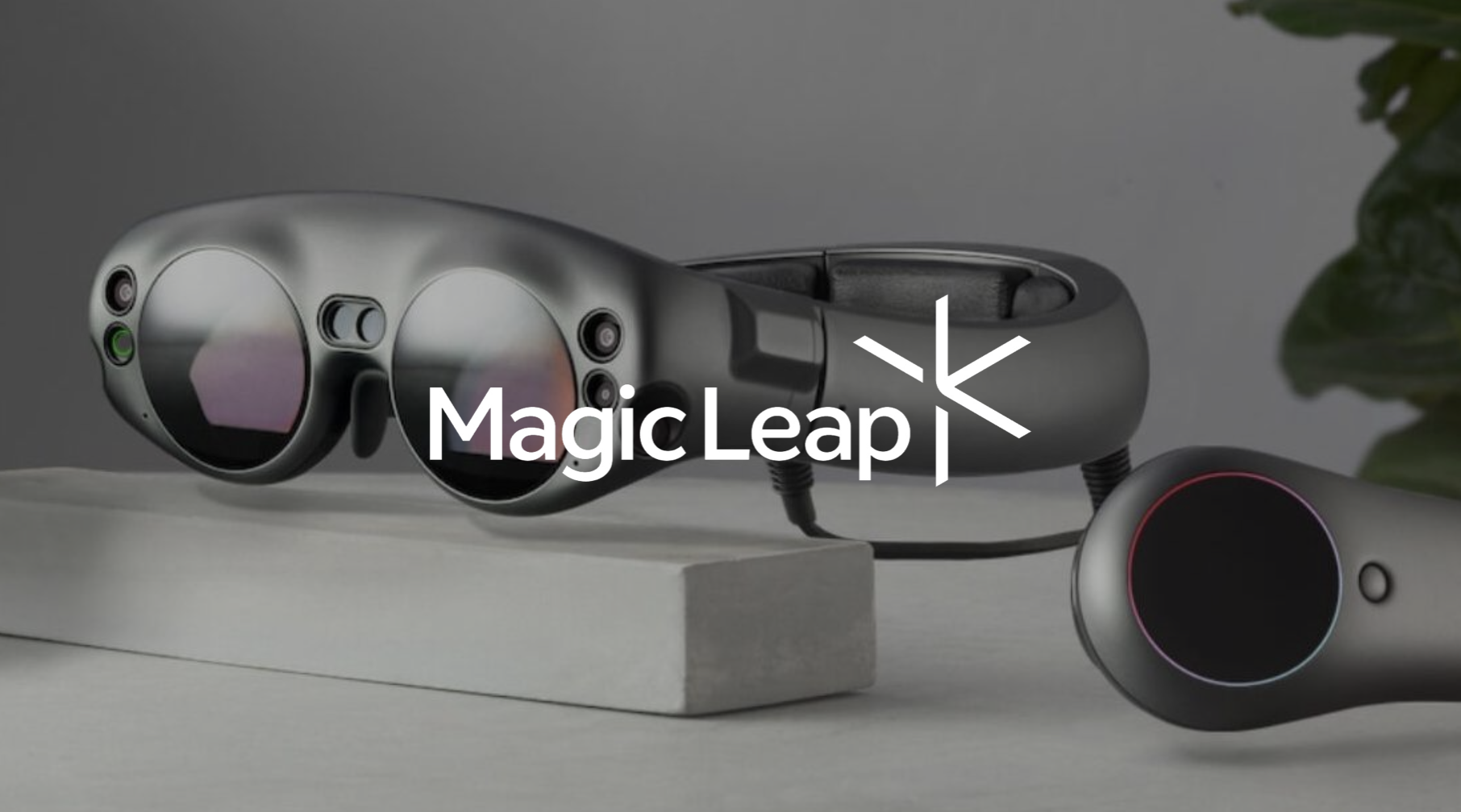 A pair of virtual reality controllers with a sleek metallic design, positioned on a light gray surface, with the Magic Leap logo layered over the image.