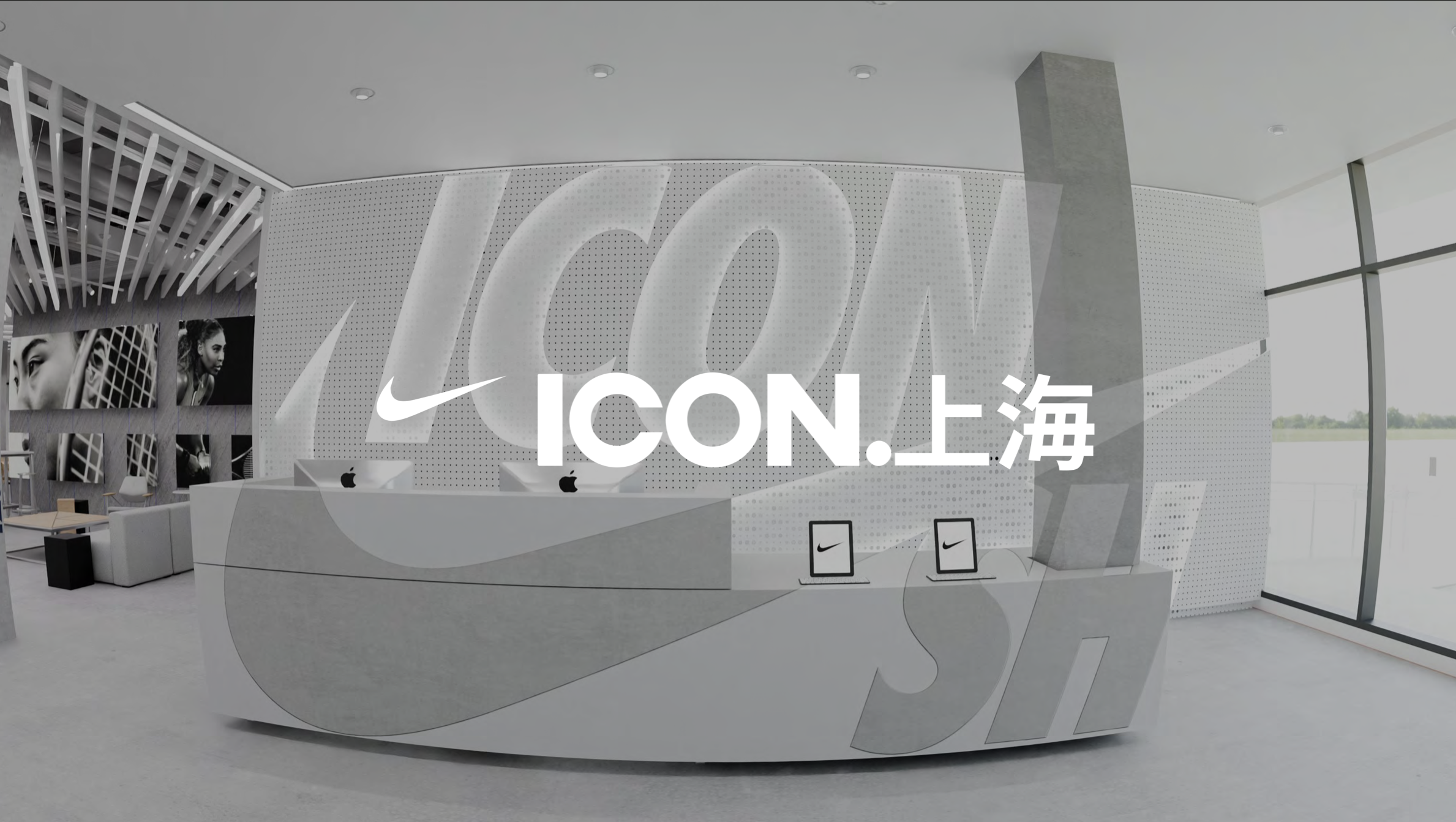 Modern reception area with Nike branding, featuring a curved desk with iMac computers, black framed Nike logos, black and white photographs of athletes on the wall, and large windows showing an outdoor landscape.