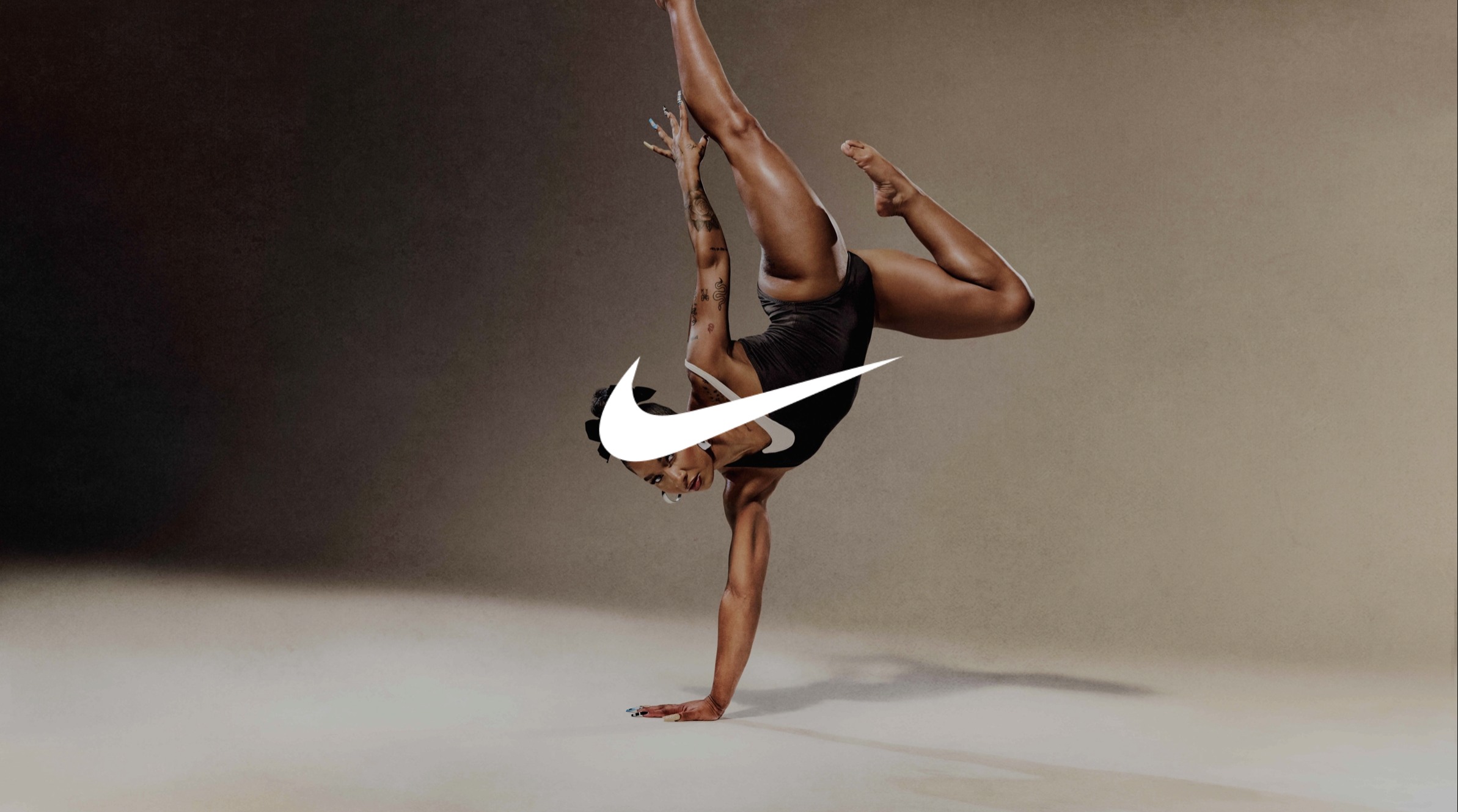 A woman in athletic wear performing a one-handed handstand with the Nike logo overlaid on her body, against a neutral background.