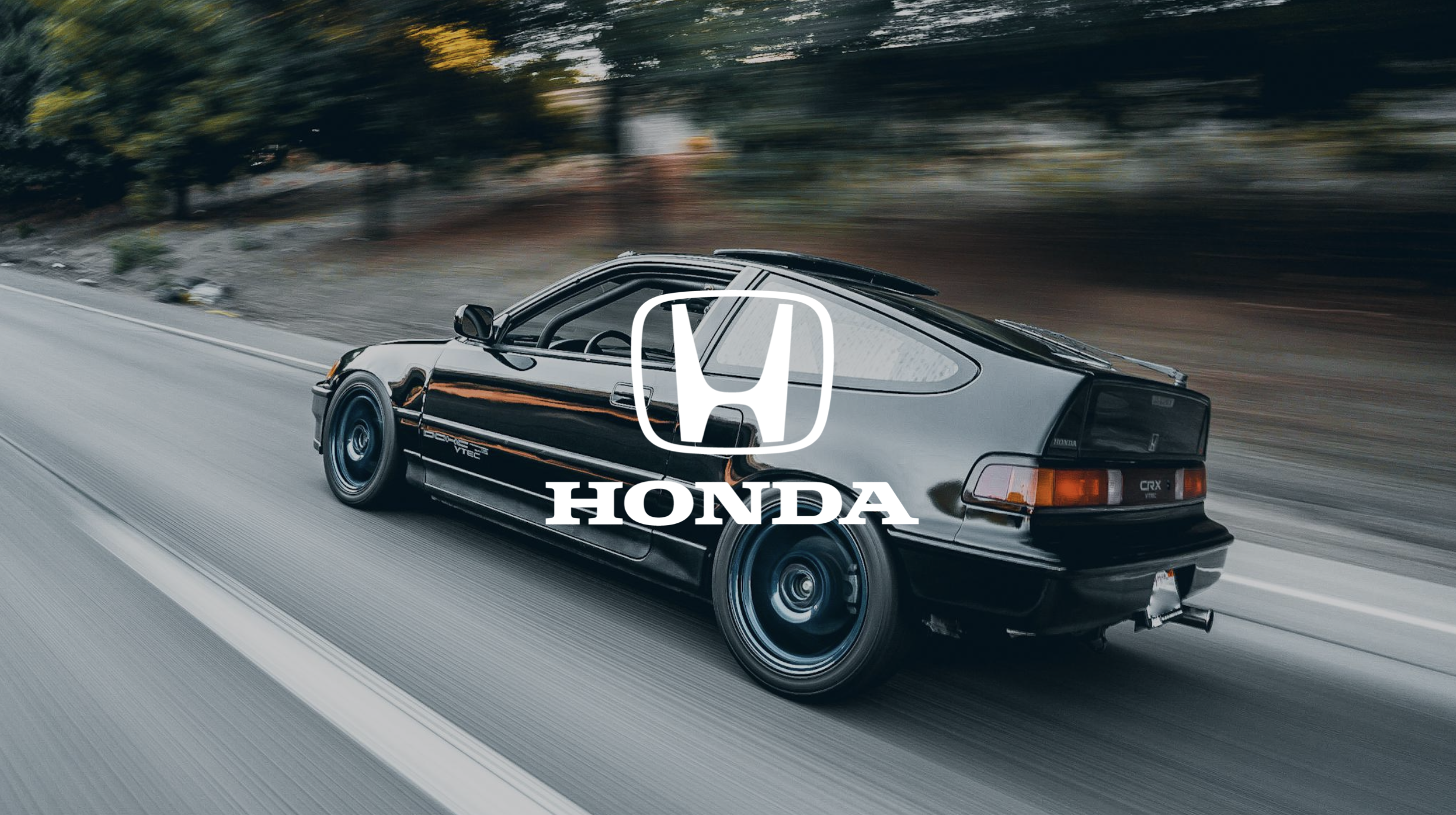 A black Honda CRX car driving on a road with a blurred background of trees, with the Honda logo and text overlayed in the center.