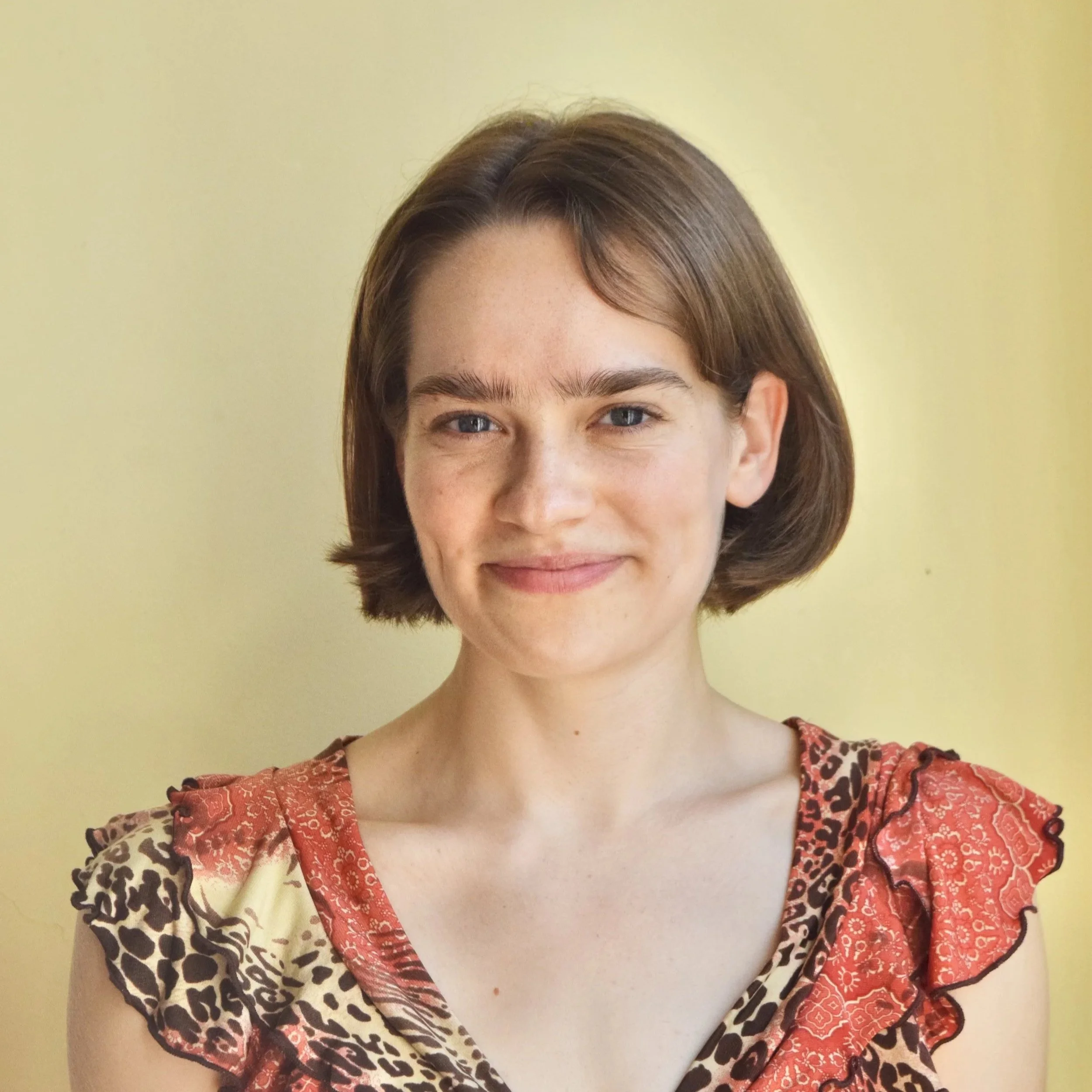 Headshot of Caitlin Durkin. She is wearing a multicolored, animal print blouse with ruffled sleeves.
