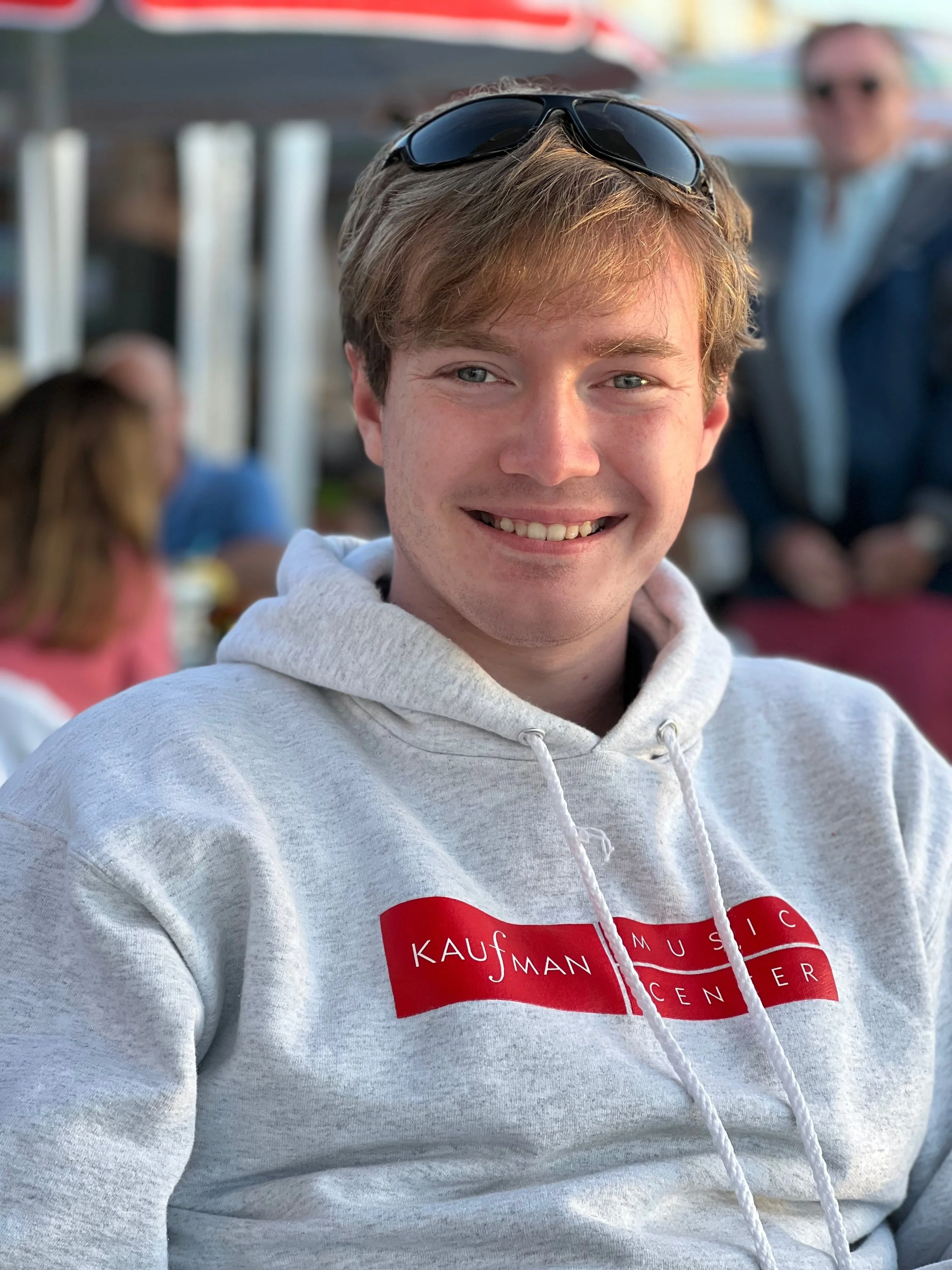 Headshot of John Wallar. He is wearing a light gray sweatshirt and has a pair of sunglasses on his head.
