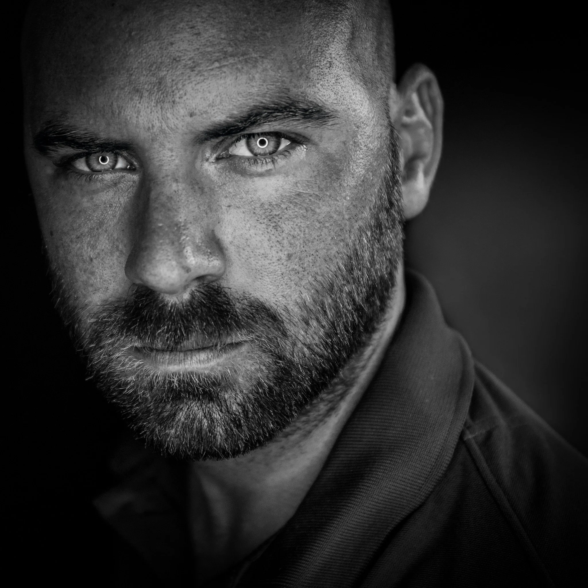 Nahaufnahme eines Mannes mit dunklem Bart und kurzen Haaren in schwarz-weiß