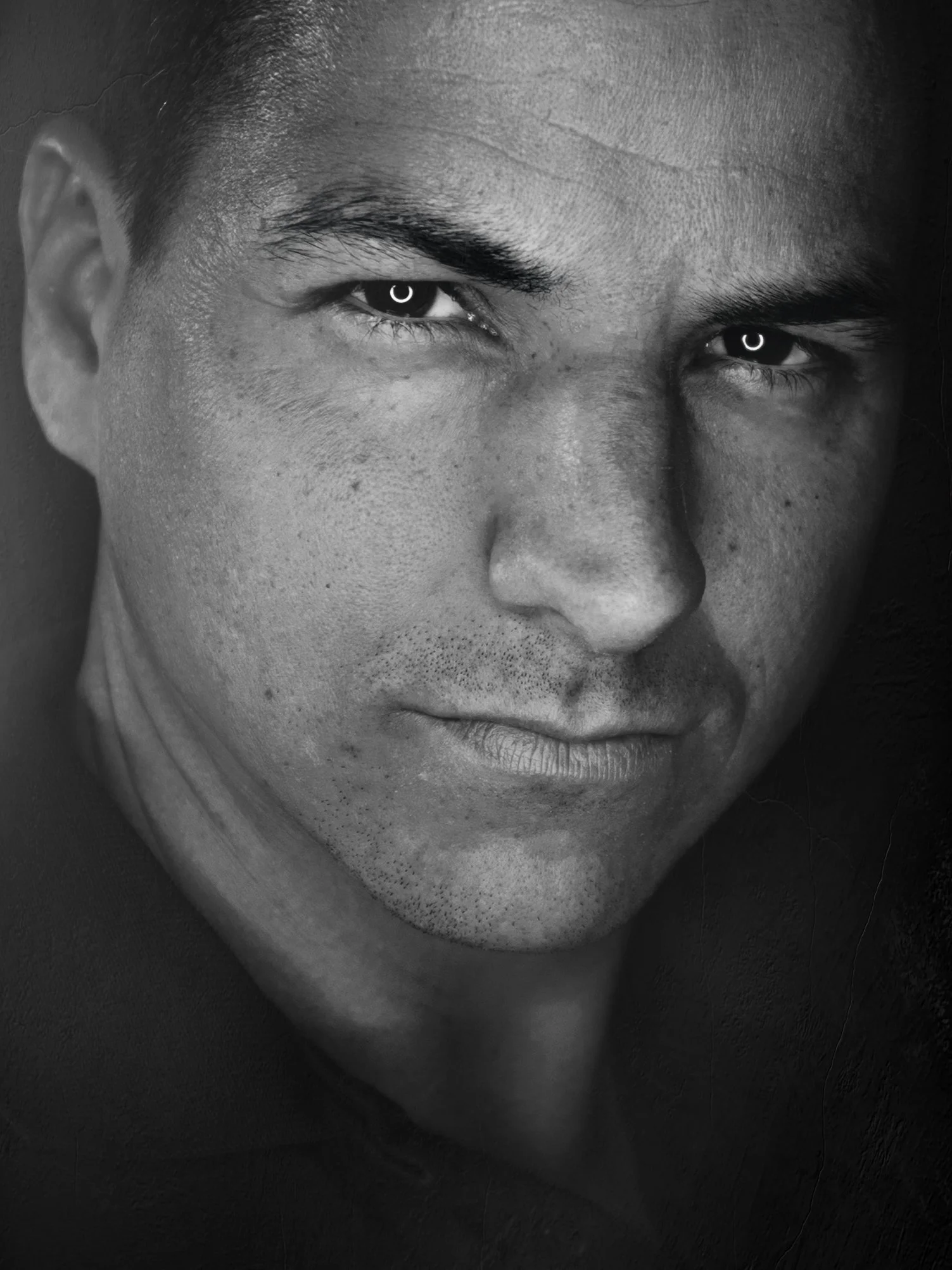 Nahaufnahme eines Mannes in Schwarz-Weiß, mit ernstem Blick und kurzen Haaren.