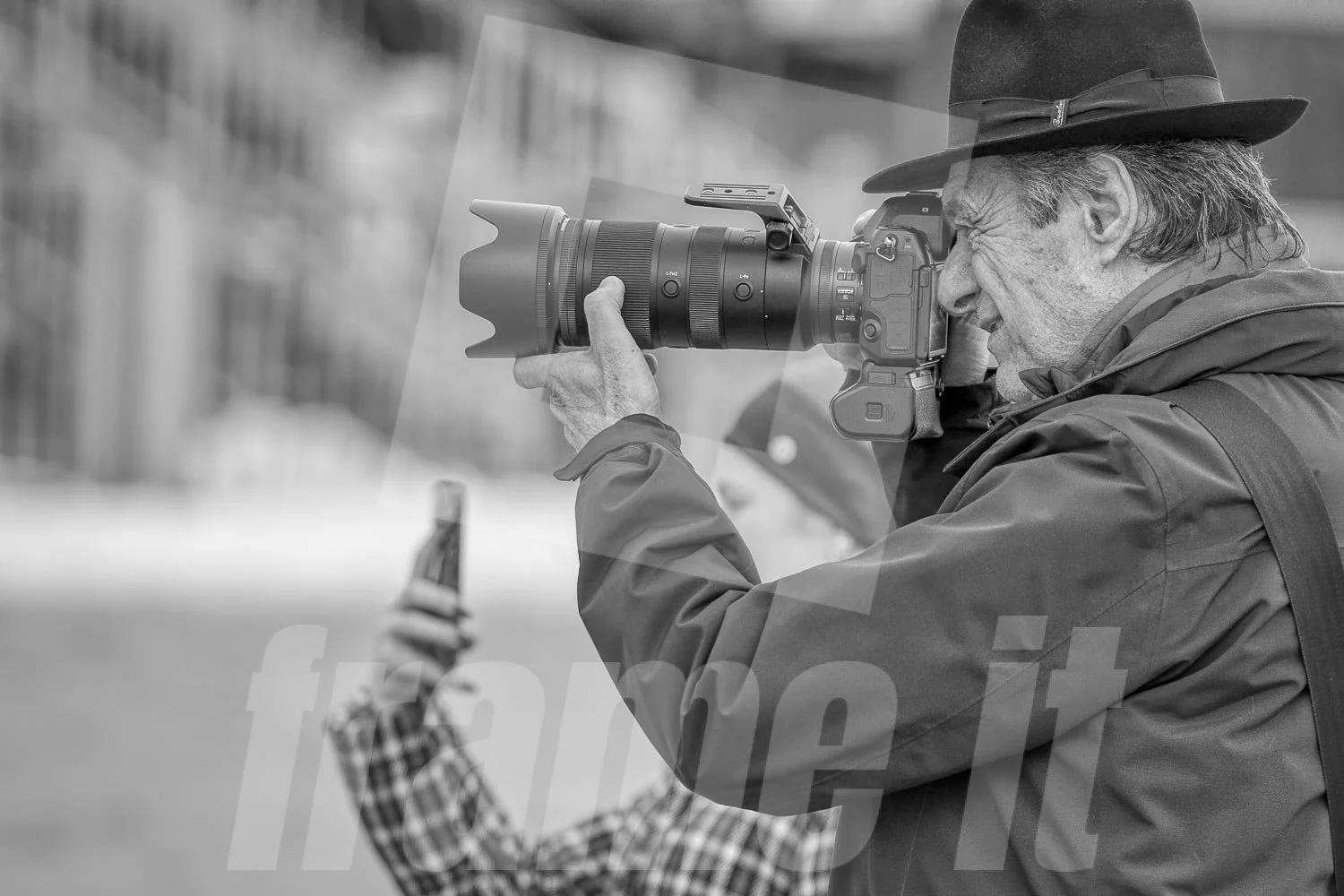 Eduard Risavy fotografiert. Im Vordergrund hält eine Person ein Smartphone hoch. Das Bild ist in Schwarzweiß.