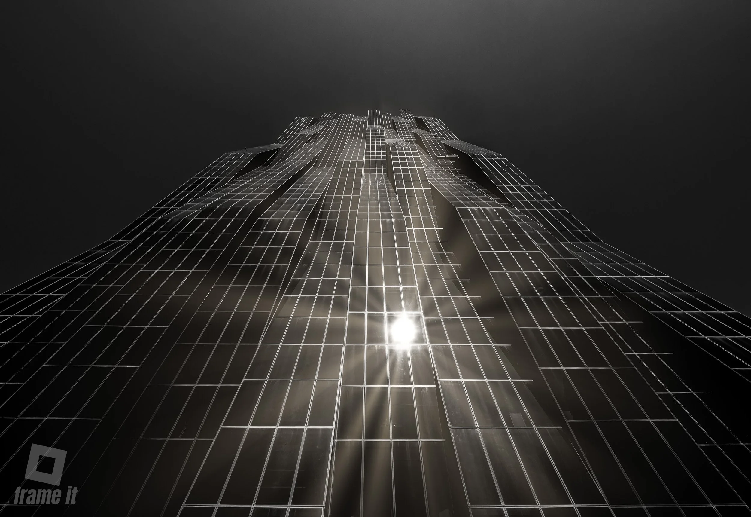 Dc Tower Wien, Moderne Glasfassade eines hohen Gebäudes, Blick von unten nach oben, reflektierende Sonnenlicht auf den Fenstern, dunkler Himmel im Hintergrund.