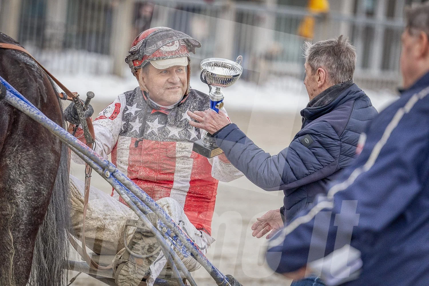 Ein Siegreicher Trabrennfahrer erhält einen Pokal von einem Mann nach einem Rennen in der Wiener Krieau.