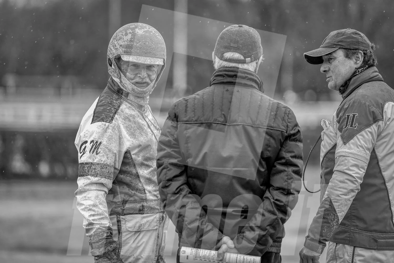 Drei Männer im Gespräch, Gerhard Mayr, Trabrennfahrer und Trabrenntrainer bei einem Rennen in der Wiener Krieau, im Hintergrund das Rennstreckengelände, schwarz-weiß Foto.
