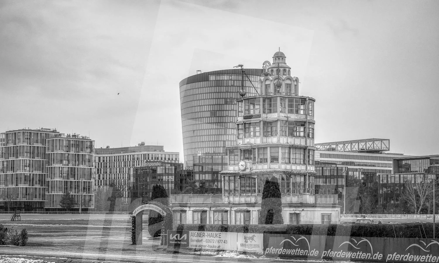 Schwarz-weiss Foto der Trabrennbahn in der Wiener Krieau., mit modernen Hochhäusern im Hintergrund und dem historischen Richterturm.