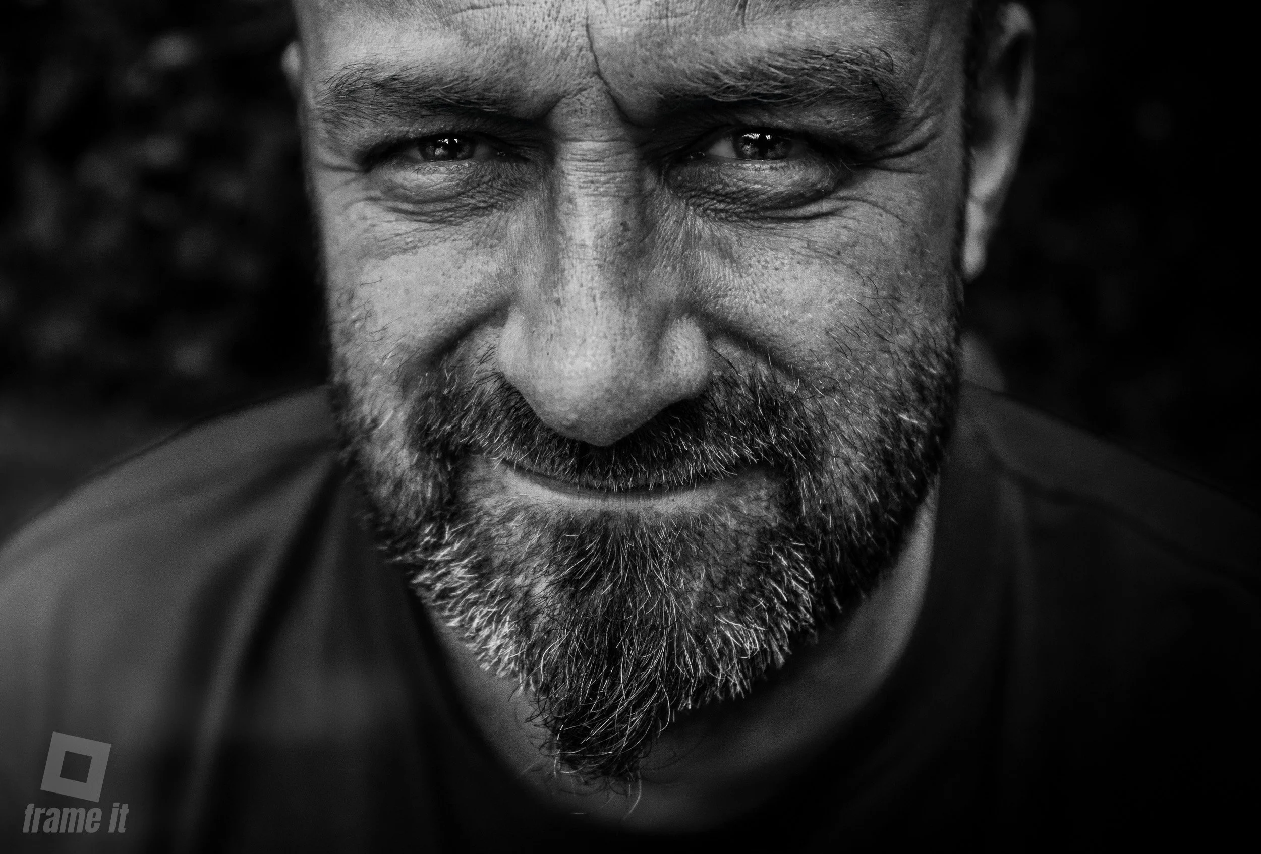 Nahaufnahme eines Mannes mit Bart, der in die Kamera blickt, schwarz-weiß.