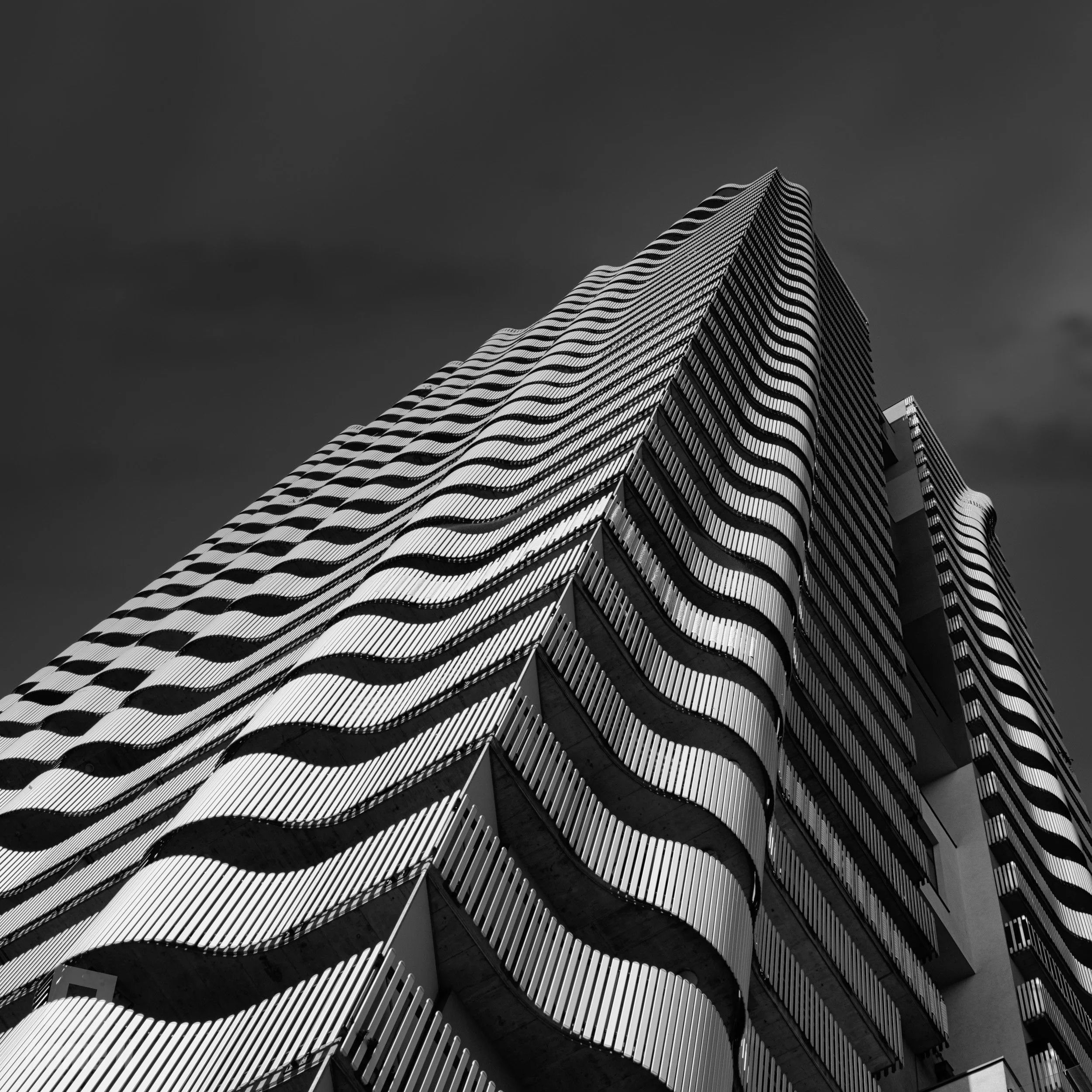 Citygate Tower in Wien - Schwarz-weiß-Foto eines hohen, modernen Hochhauses mit wellenförmig gestalteten Balkonen gegen dunklen Himmel.