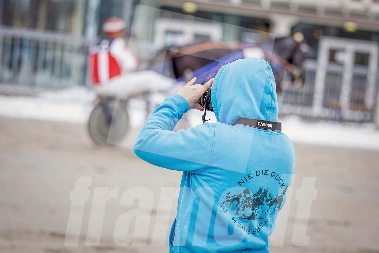 Person in blauer Kapuzenjacke fotografiert bei Regenwetter einen Trabrennfahrer.