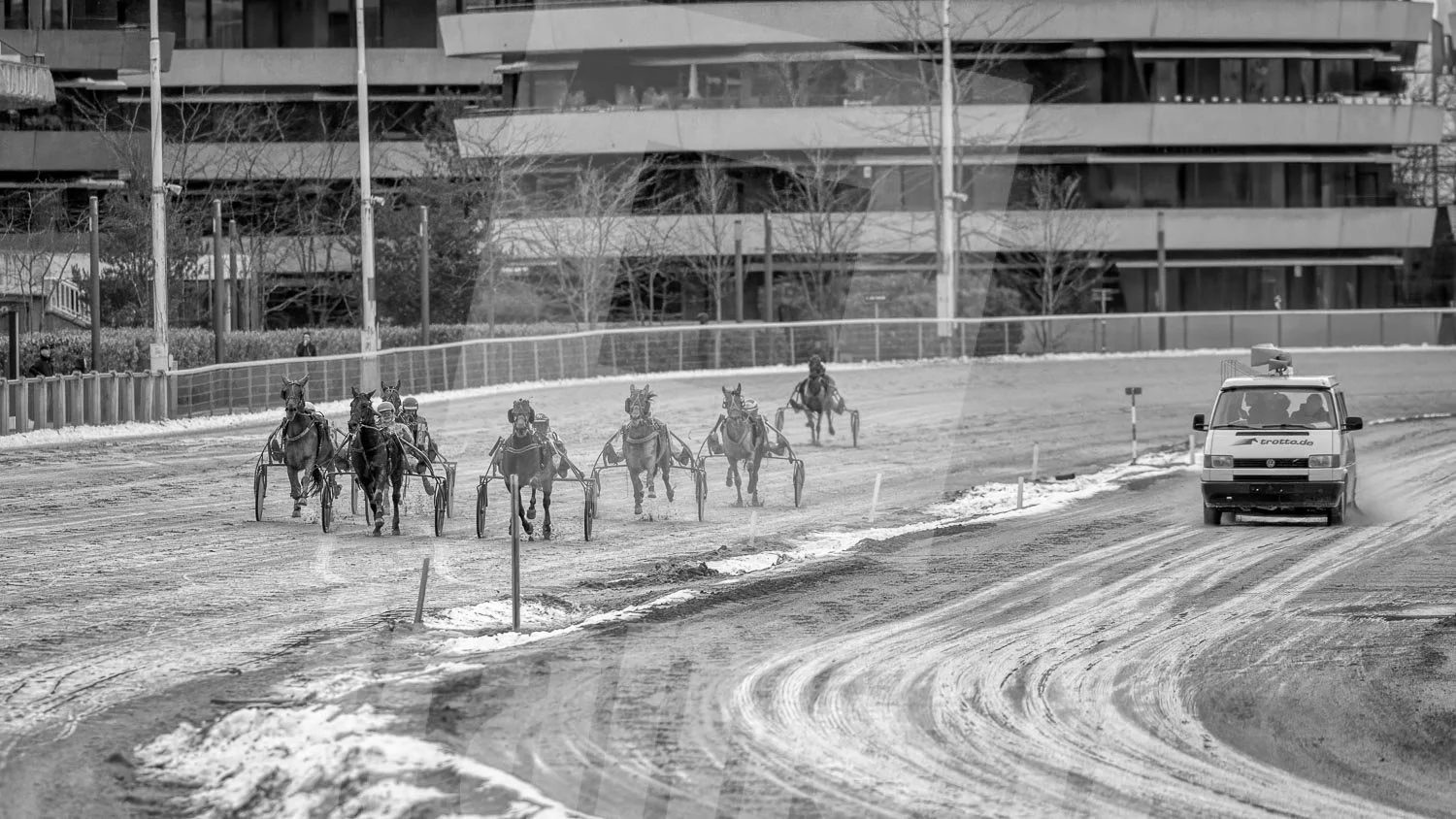 Pferderennen der Trabrennbahn in der Wiener Krieau, im Hintergrund moderne Gebäude, im Vordergrund Schneeflecken.