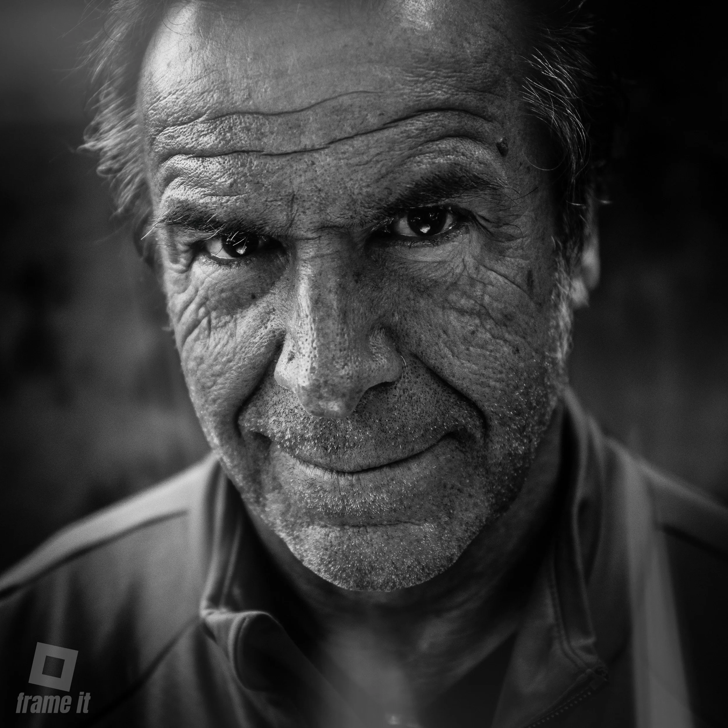 Nahaufnahme eines älteren Mannes mit dunkler Haut, grauem Haar und markanten Gesichtszügen, in Schwarzweiß aufgenommen.