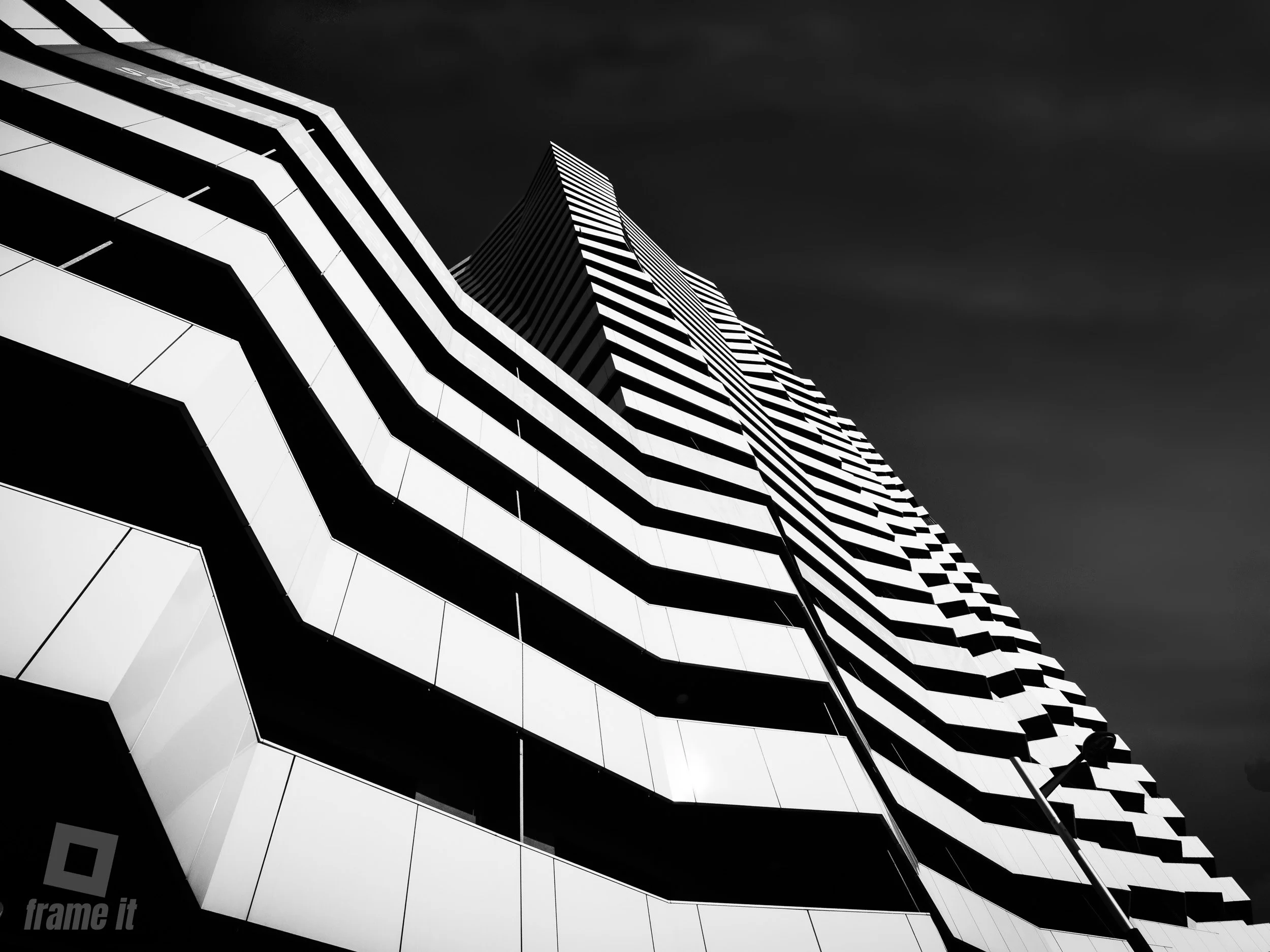 Schwarz-weiß-Foto eines modernen, hohen Gebäudes, der Leopoldtower,  mit geometrischem Design und schrägen Linien gegen einen dunklen Himmel.