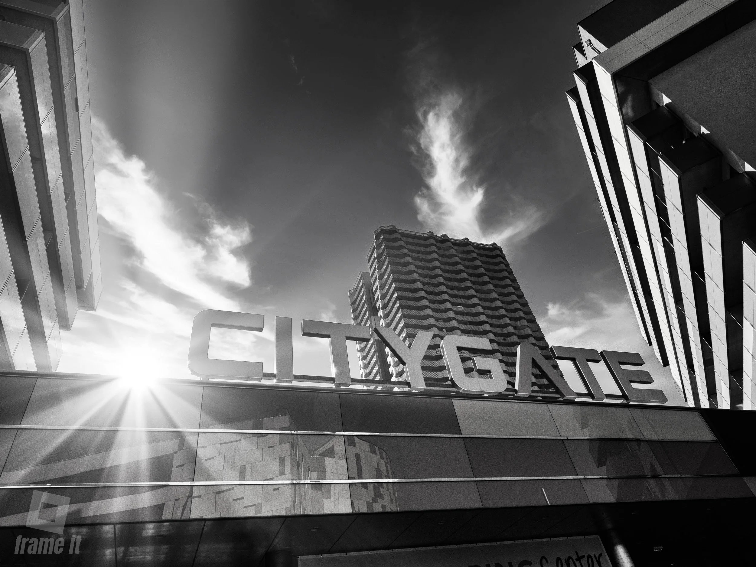 Schwarz-weißaufnahme  mit modernen hohen Gebäuden und einem Schild mit der Aufschrift "CITY GATE" vor der Sonne.