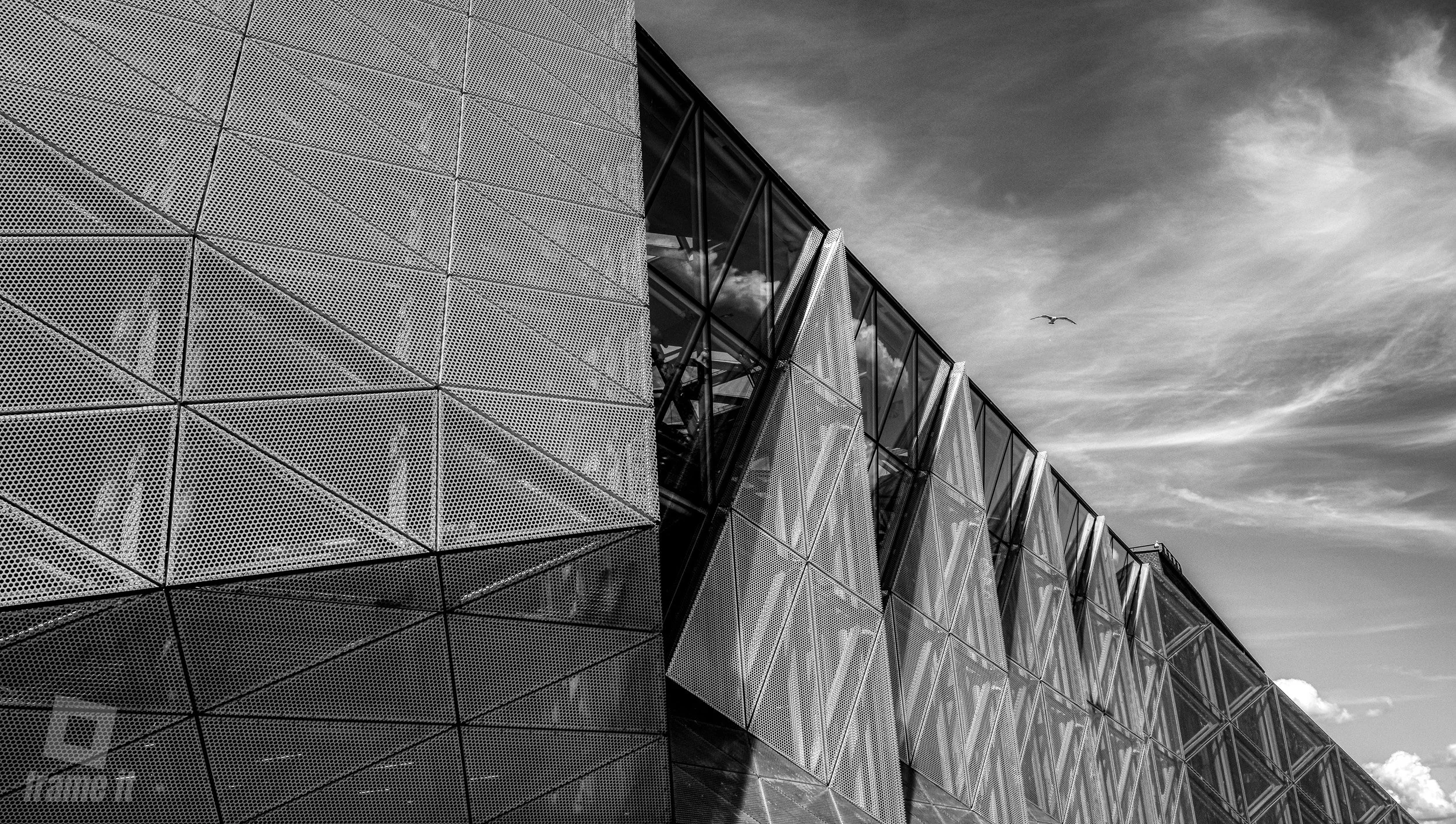 Stadtmuseum Helsingør - Gebäude mit perforierten Metallfassaden und großen Glasfenstern, ein Vogel fliegt am Himmel, in Schwarz-Weiß-Fotografie.